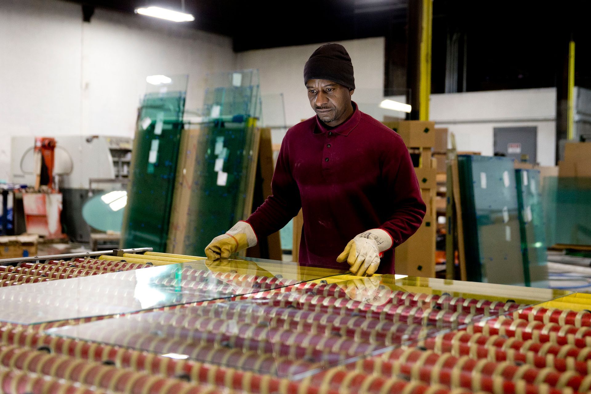 Man in work gloves inspecting glass sheets in a factory.