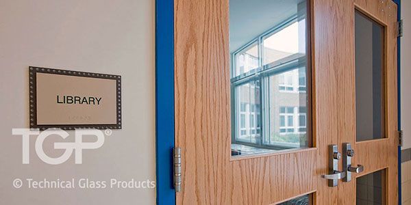 A library sign and wooden door with glass panels reflect a building's exterior.