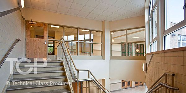 Staircase and hallway in a building with beige walls and natural light shining through windows.