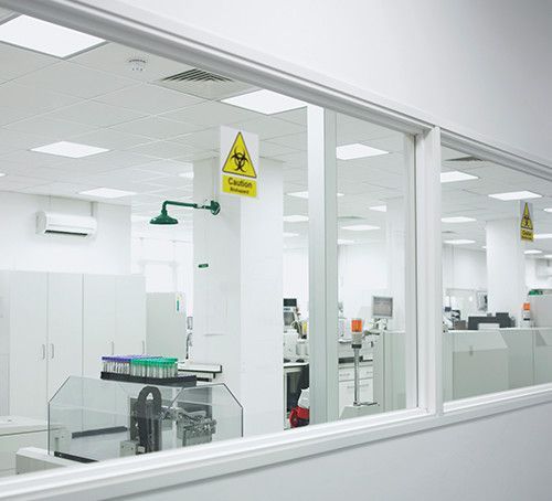 Inside a sterile white lab, seen through a window. A biohazard sign hangs.