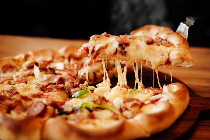 Pizza slice with melted cheese lifted from a whole pizza.