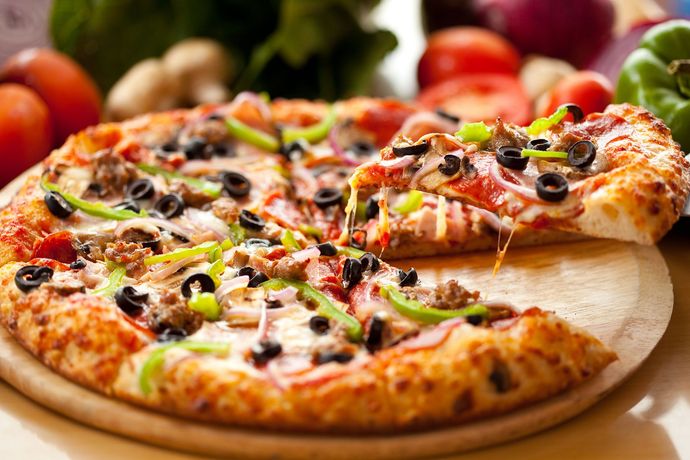 Pizza with olives, peppers, and sausage; a slice being lifted from the pie.