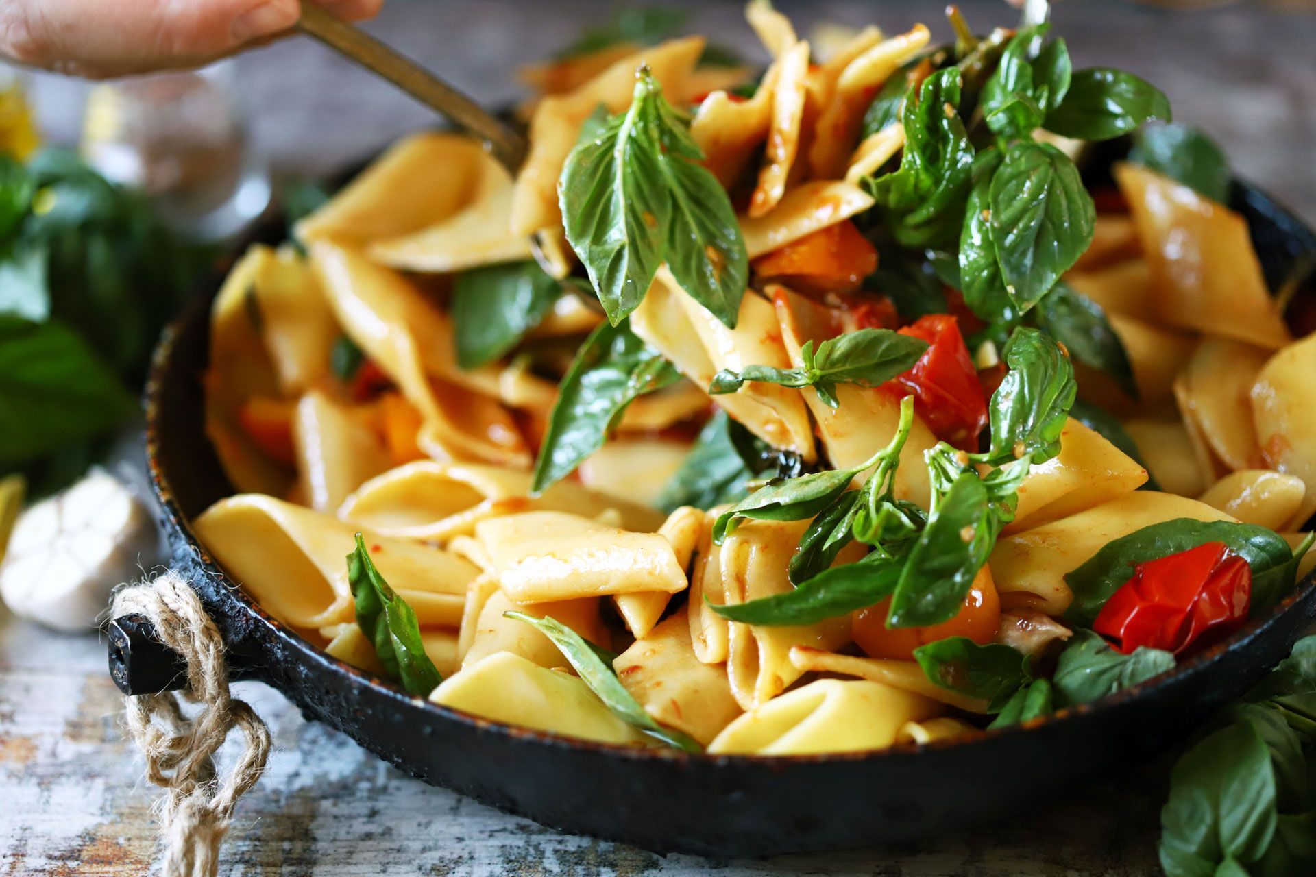 Pasta with tomatoes and basil in a black pan, being served with a spoon.