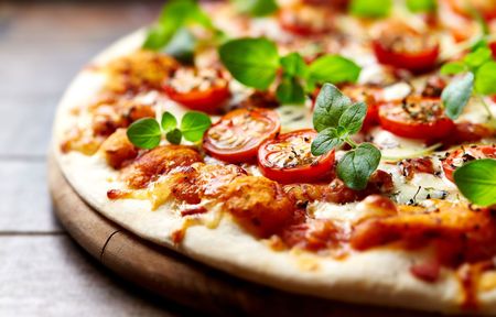 Pizza with tomatoes, herbs, and cheese on a wooden board.