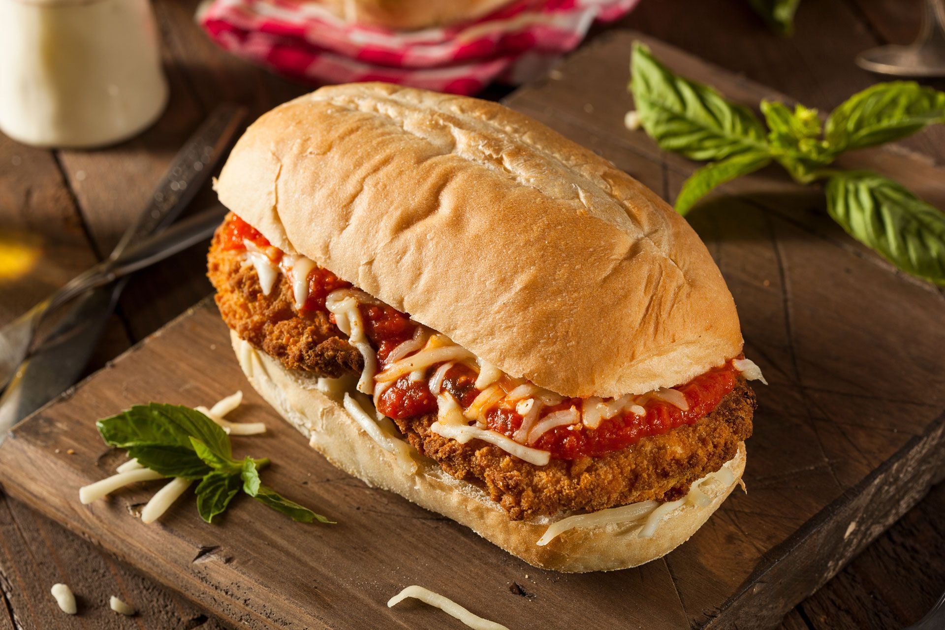 Chicken parmesan sandwich on a wooden board, with sauce and cheese.