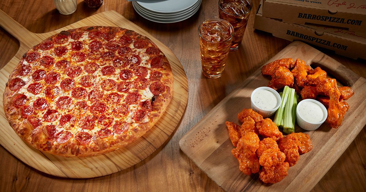 Pepperoni pizza, buffalo wings, drinks, and dipping sauces on wooden boards.