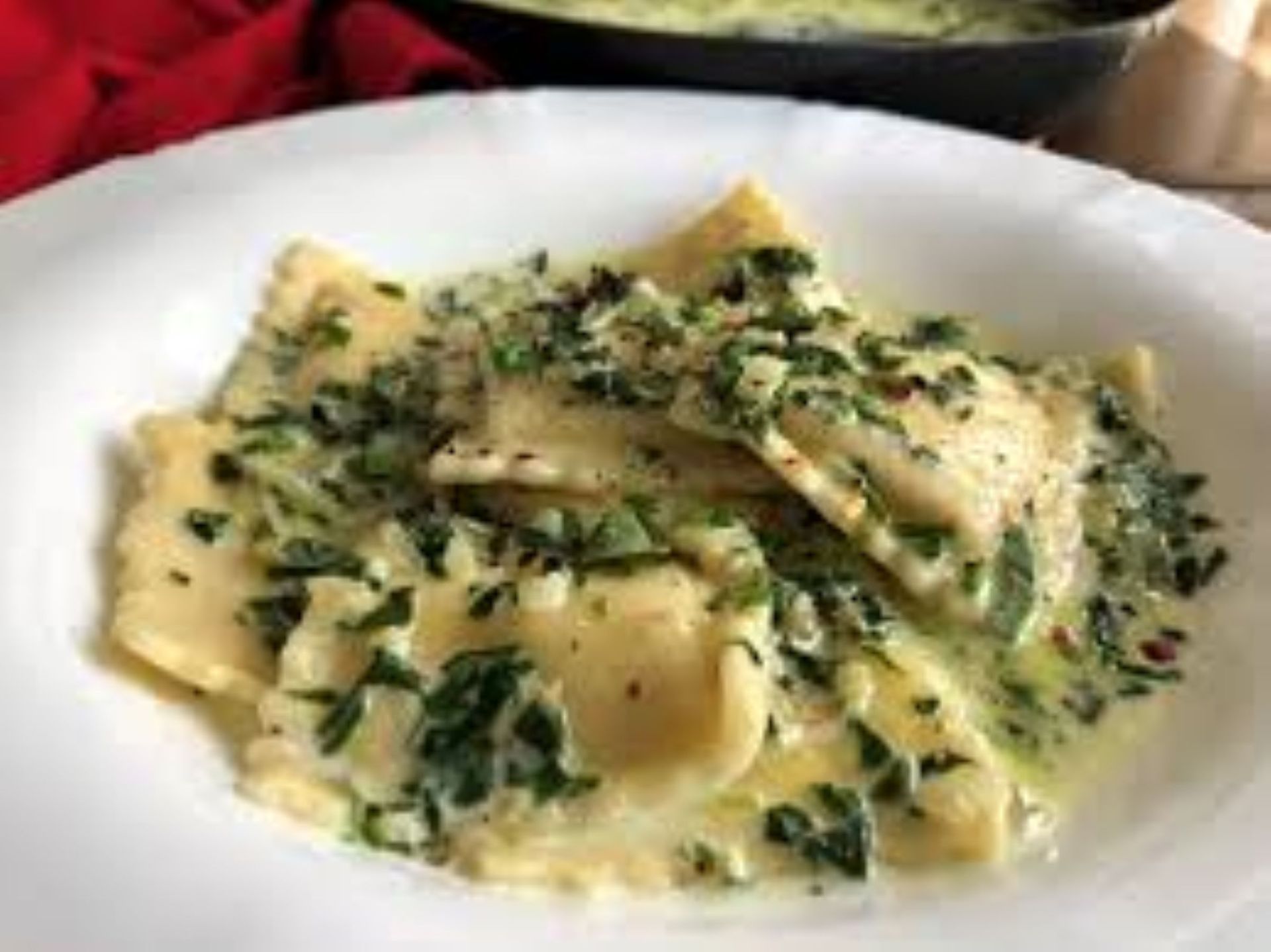 Ravioli in creamy sauce with chopped green herbs in a white bowl.