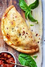 Calzone on parchment with tomato sauce and basil.
