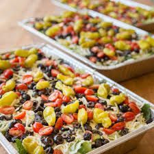 Three rectangular trays of layered salad with yellow peppers, tomatoes, and olives.