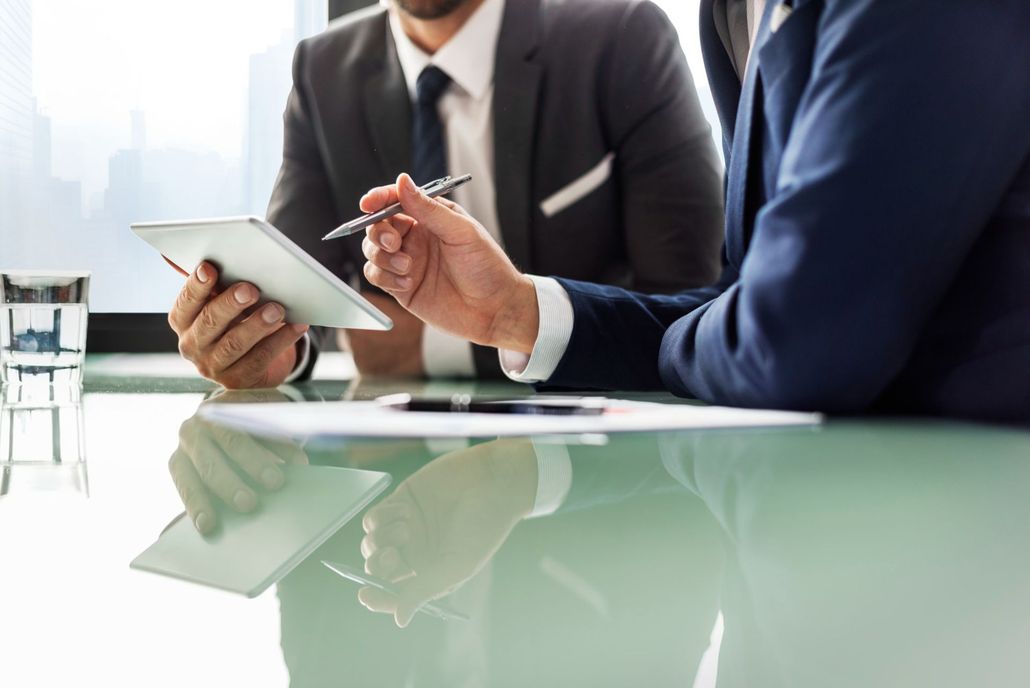 Two men are sitting at a table looking at a tablet.
