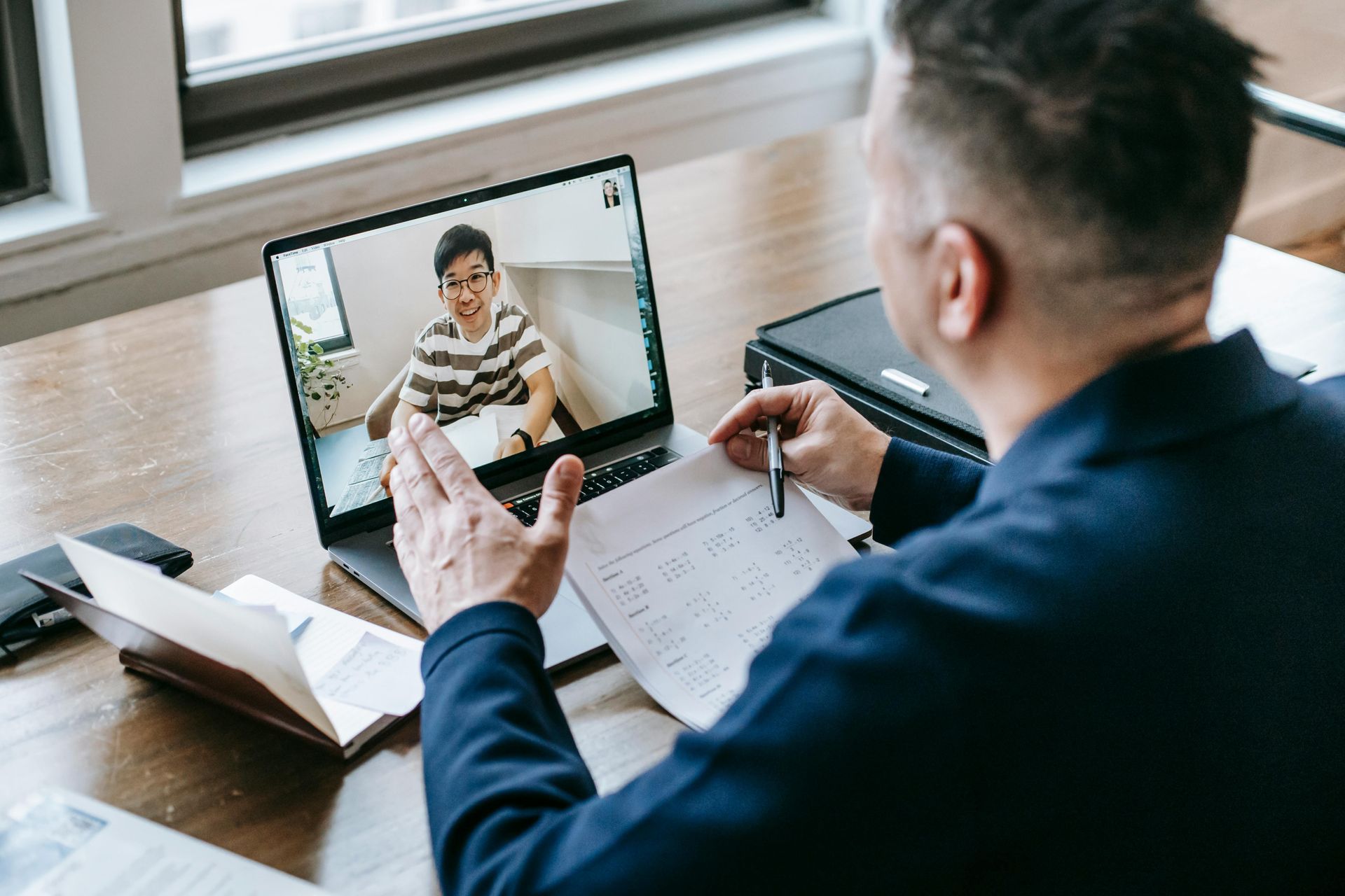 A man is sitting at a desk using a laptop computer to have a video call with a woman.
