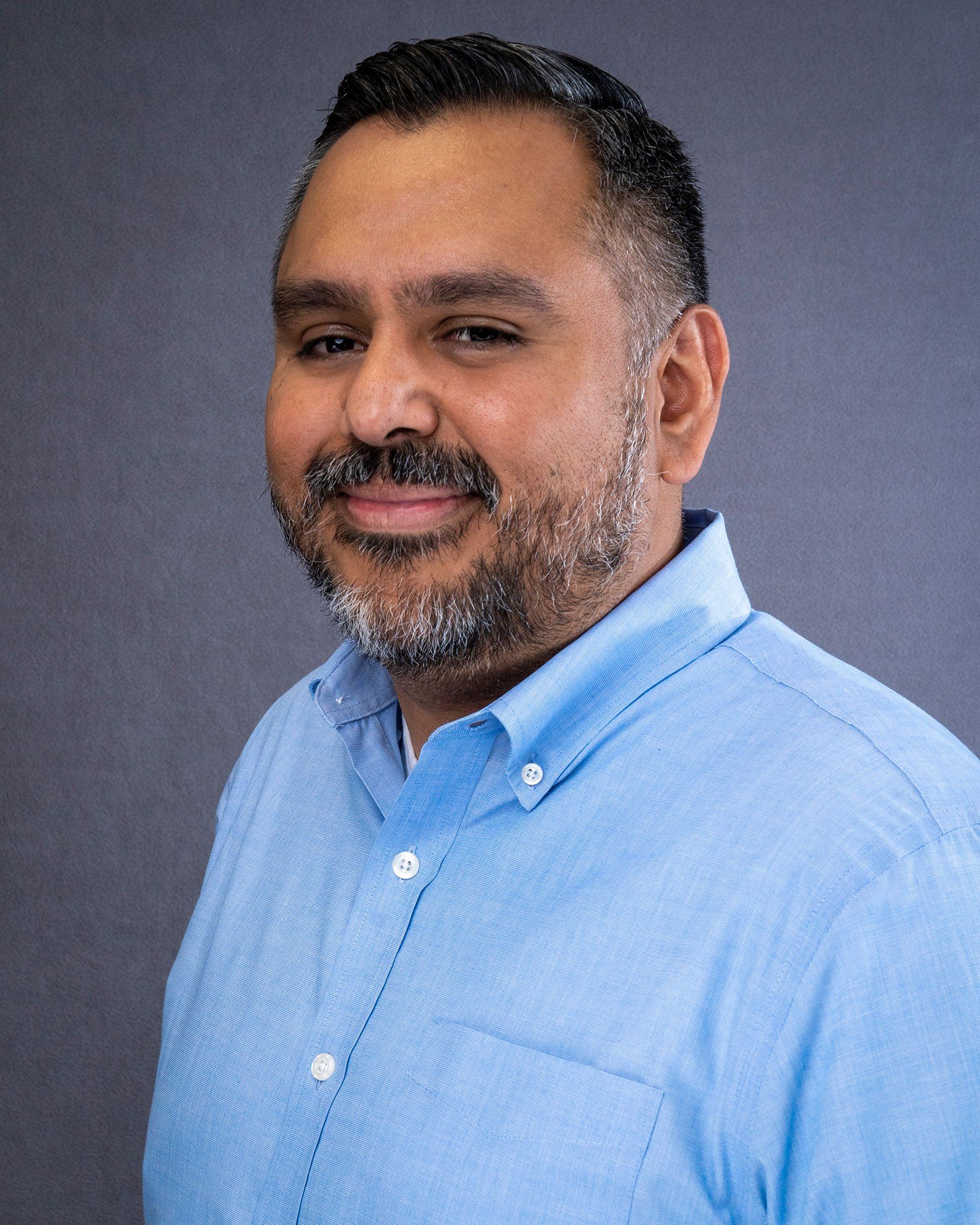 a man with a beard is wearing a blue shirt and smiling for the camera .