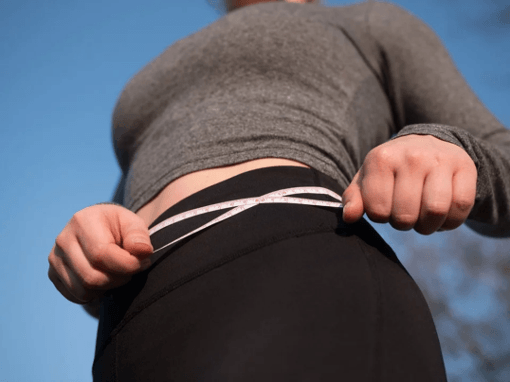 a woman is measuring her waist with a tape measure .