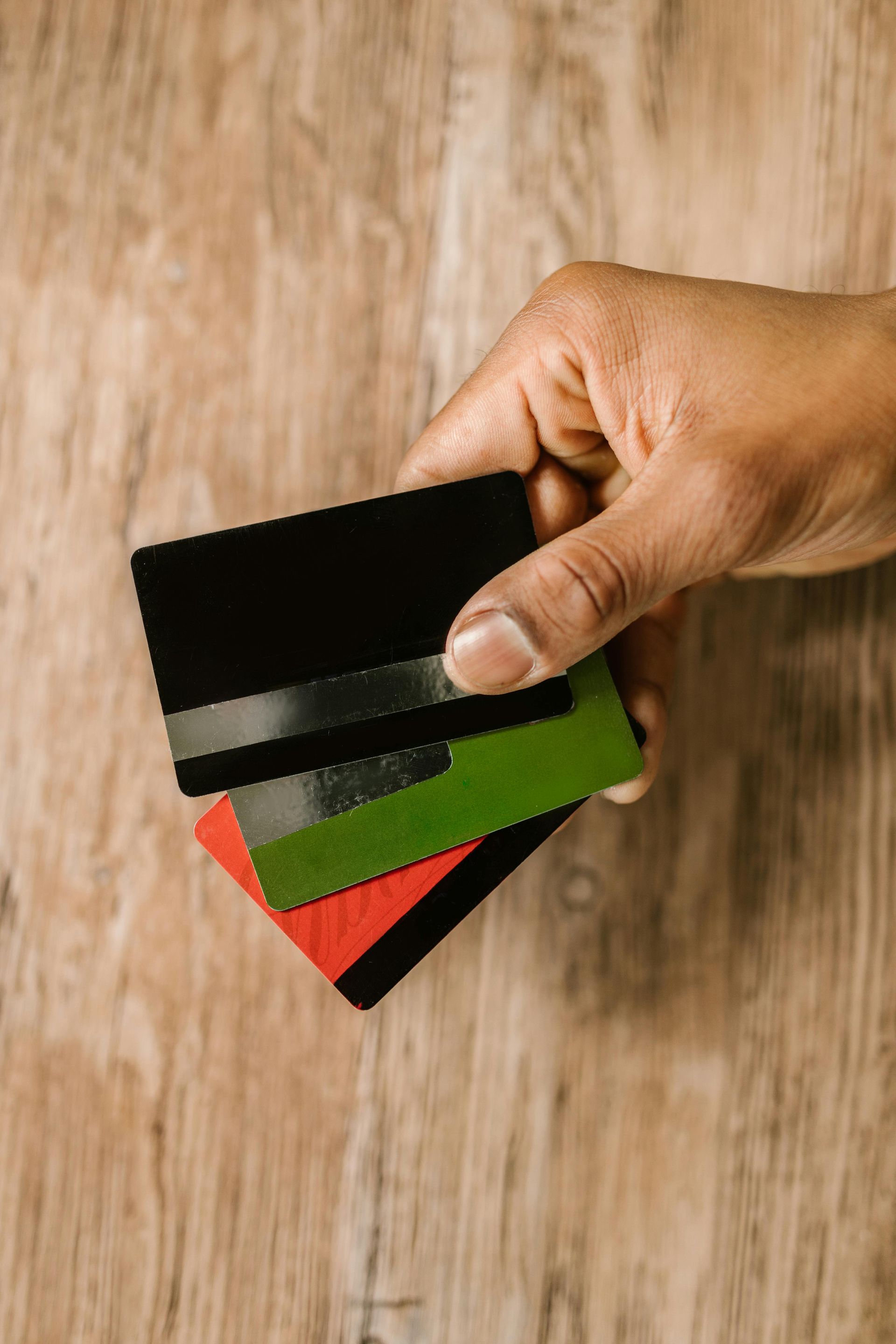 Mano che tiene una pila di tre carte colorate: nero, verde e rosso, su una superficie di legno.