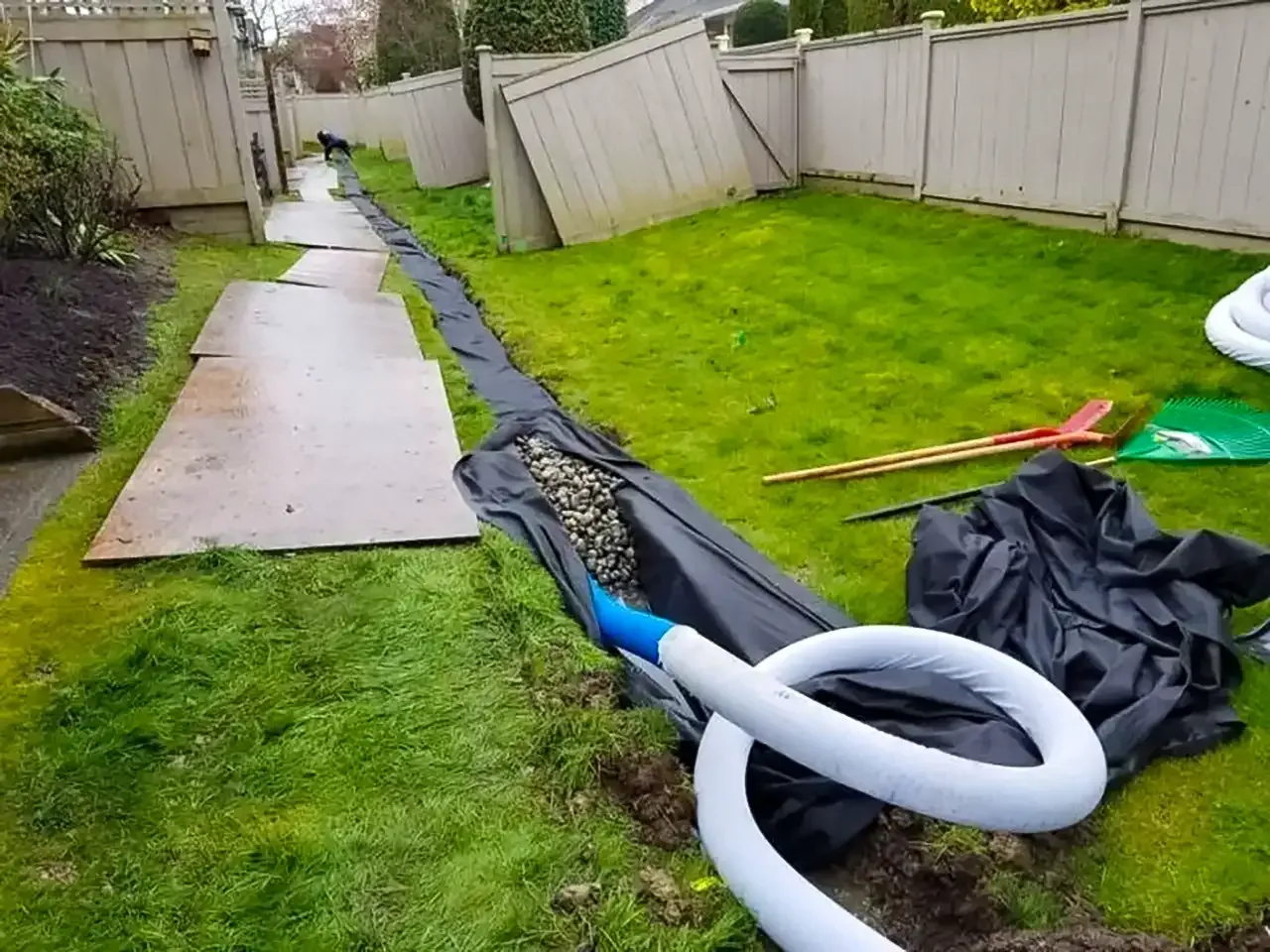 A hose is lying on the ground in a backyard next to a fence.