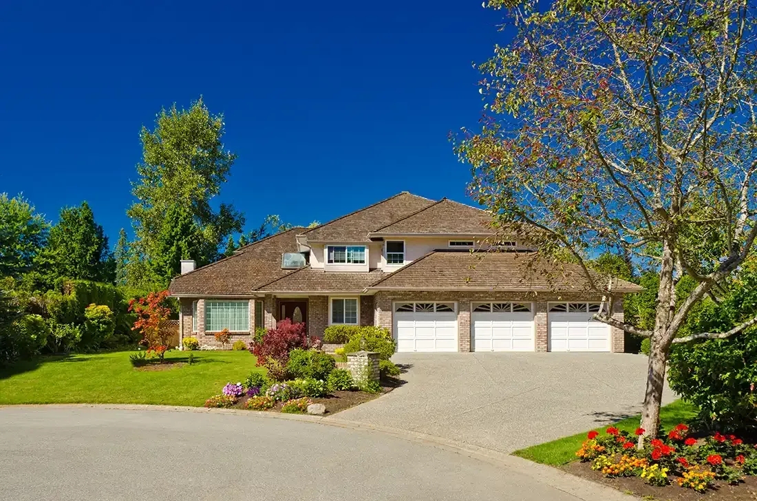 A large house with three garage doors sits on top of a lush green lawn.