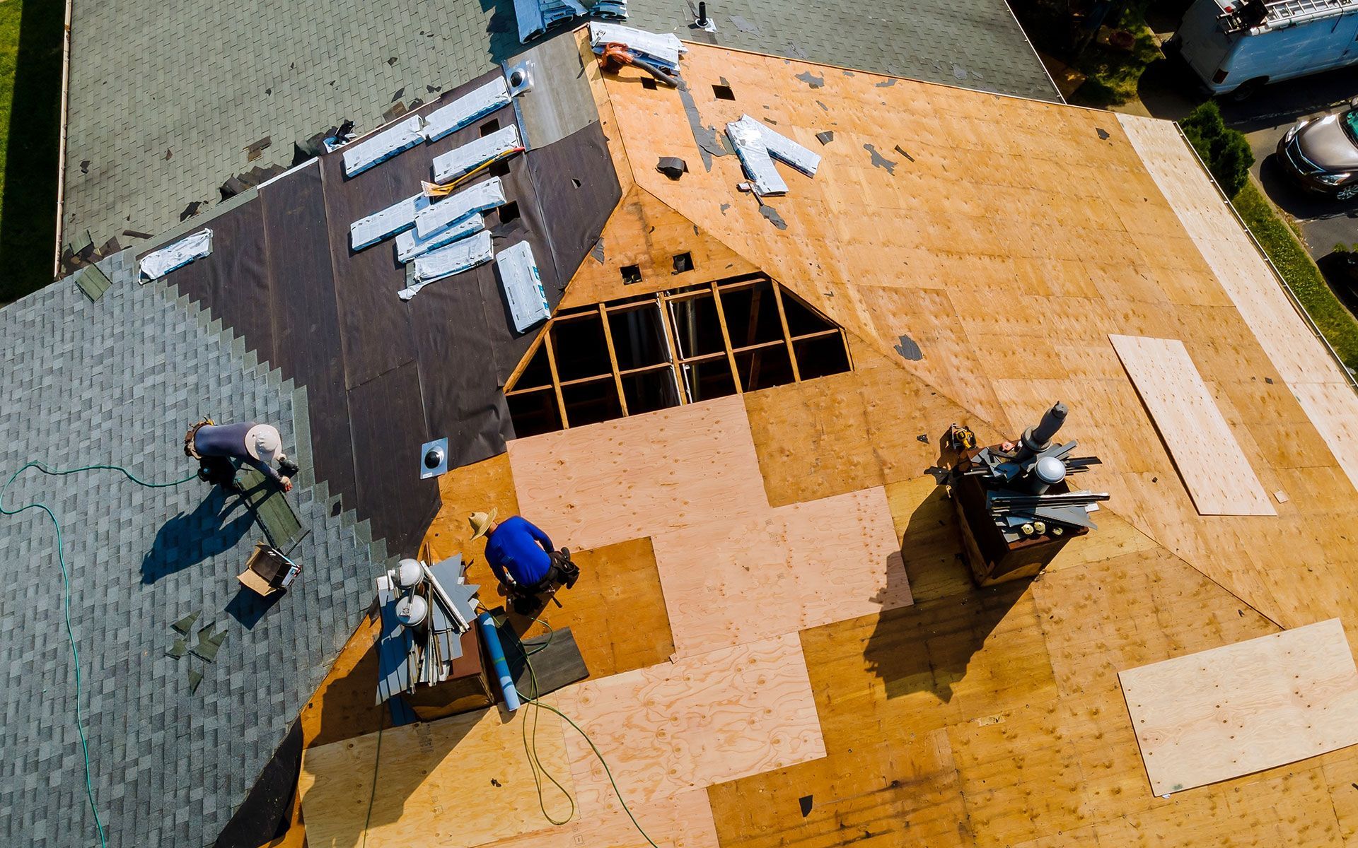 Roofers working on a house roof with exposed plywood and new shingles, aerial view.