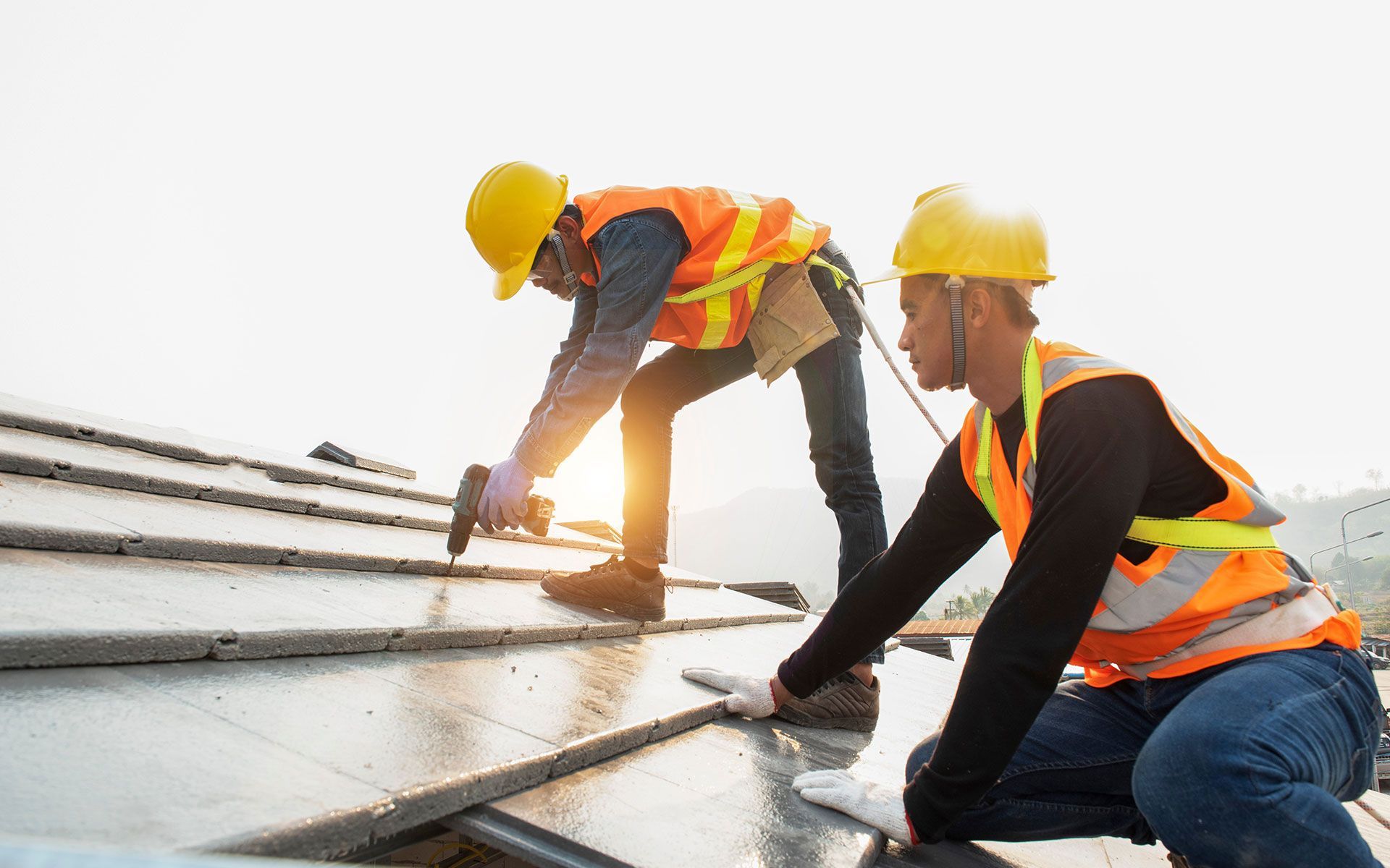 Two roofers installing solar panels on a rooftop, wearing safety vests and hard hats in bright sunlight.