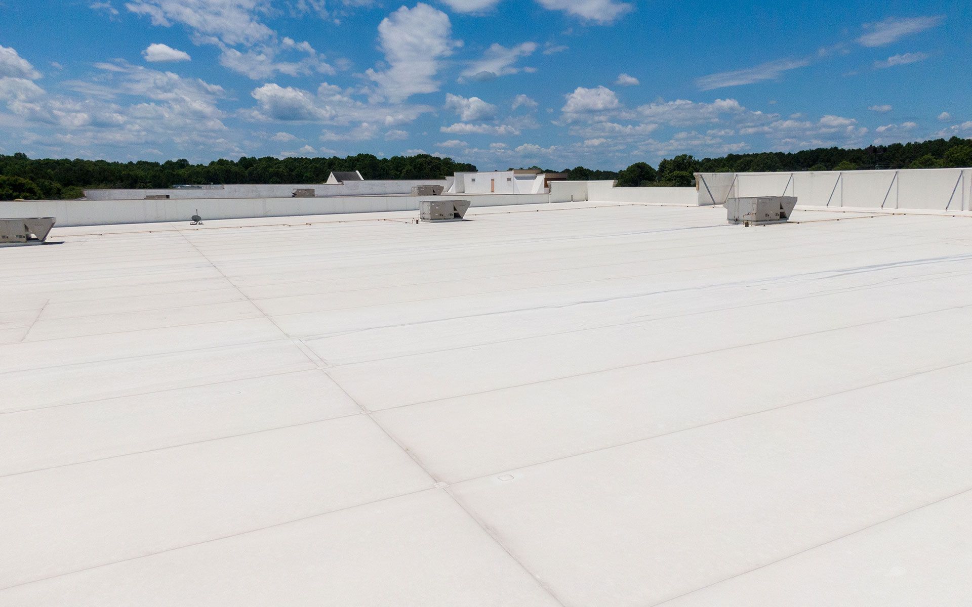 White commercial roof with HVAC units against a blue sky with puffy clouds.