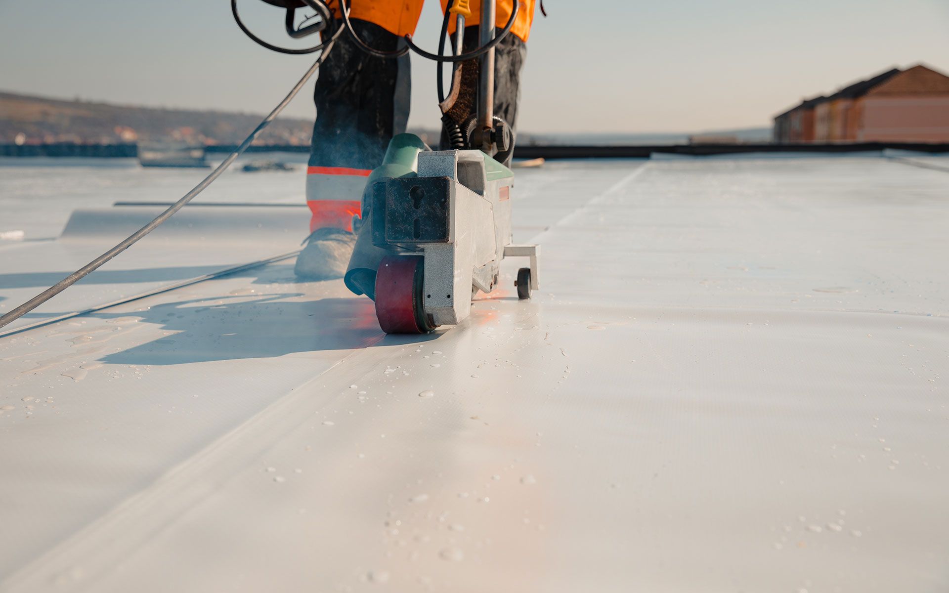 A worker welding white roofing material with an industrial machine on a rooftop under a blue sky.