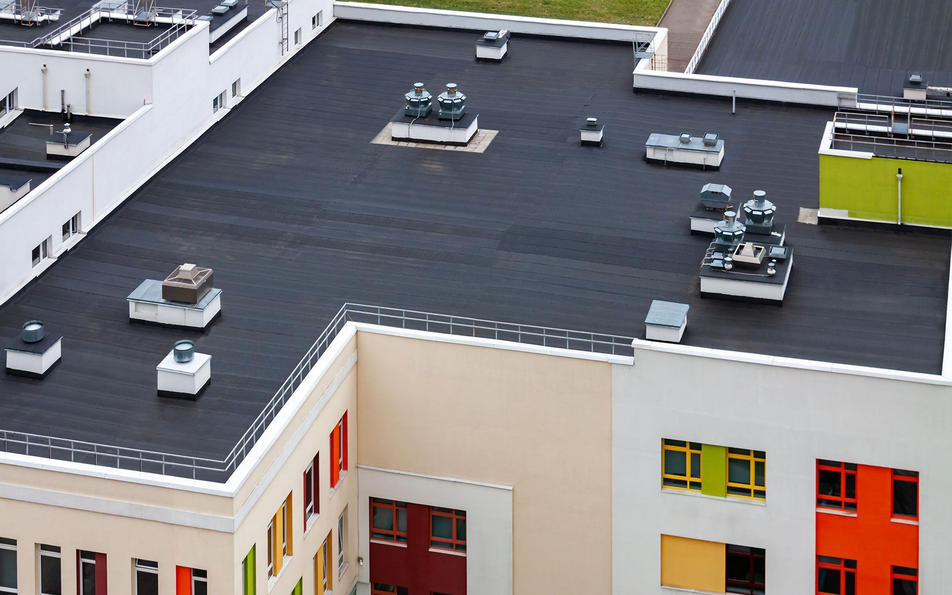 A flat, black rooftop of a building with multiple ventilation units and colorful windows.