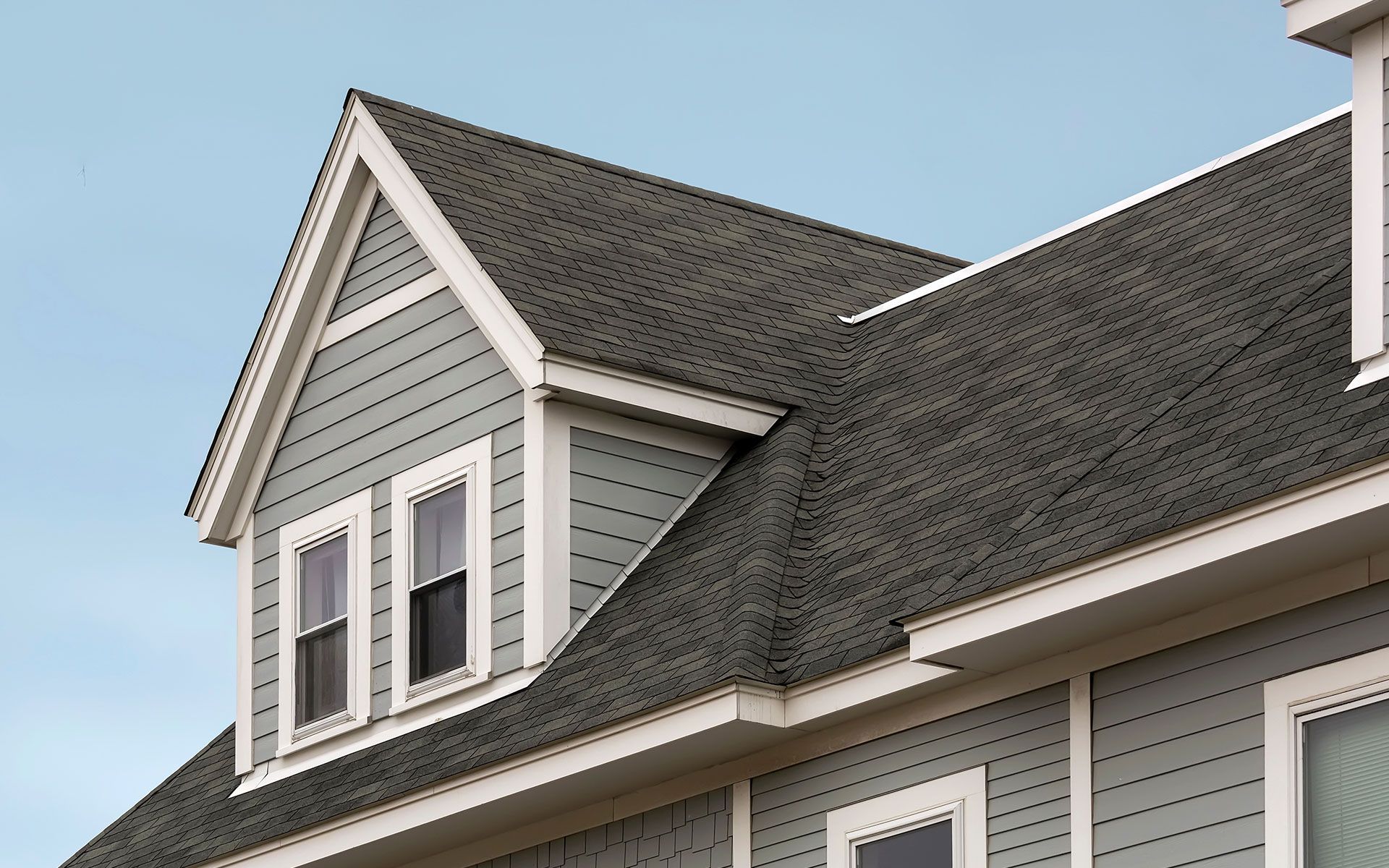 Close-up of a house with gray roof, blue siding, and white trim. Two windows in the triangular gable.