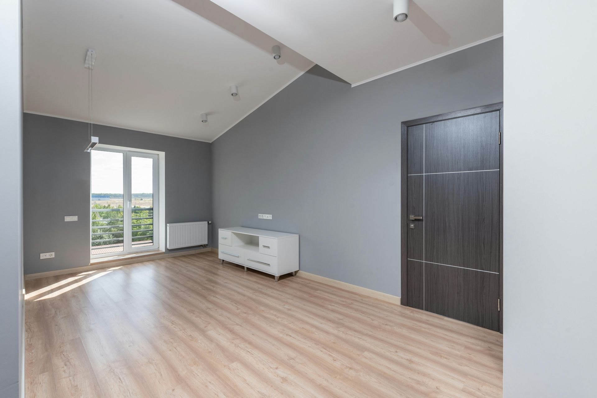 Empty gray living room with wood flooring, large windows, white radiator, and dark closet doors