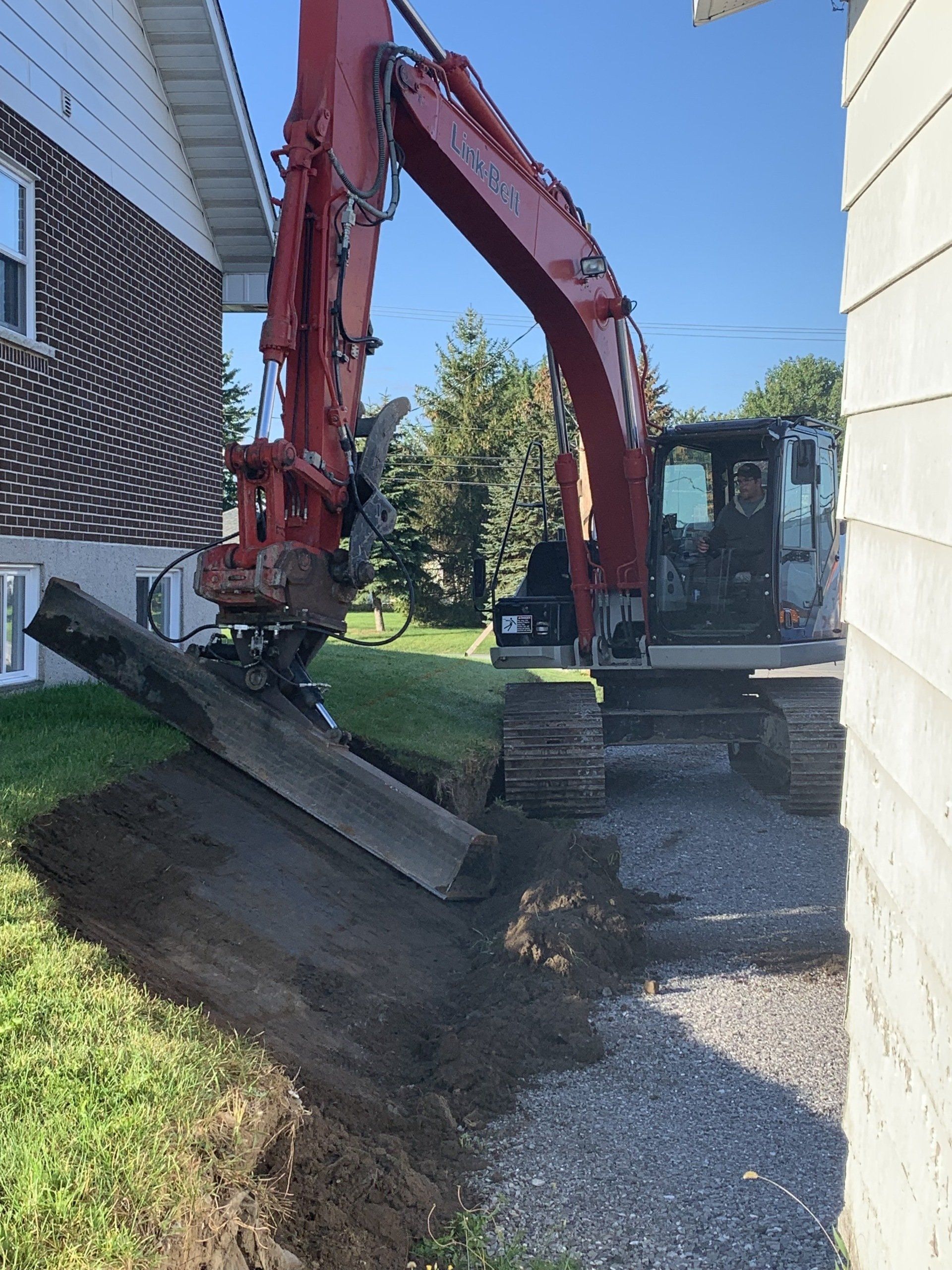 Une excavatrice creuse un trou devant une maison