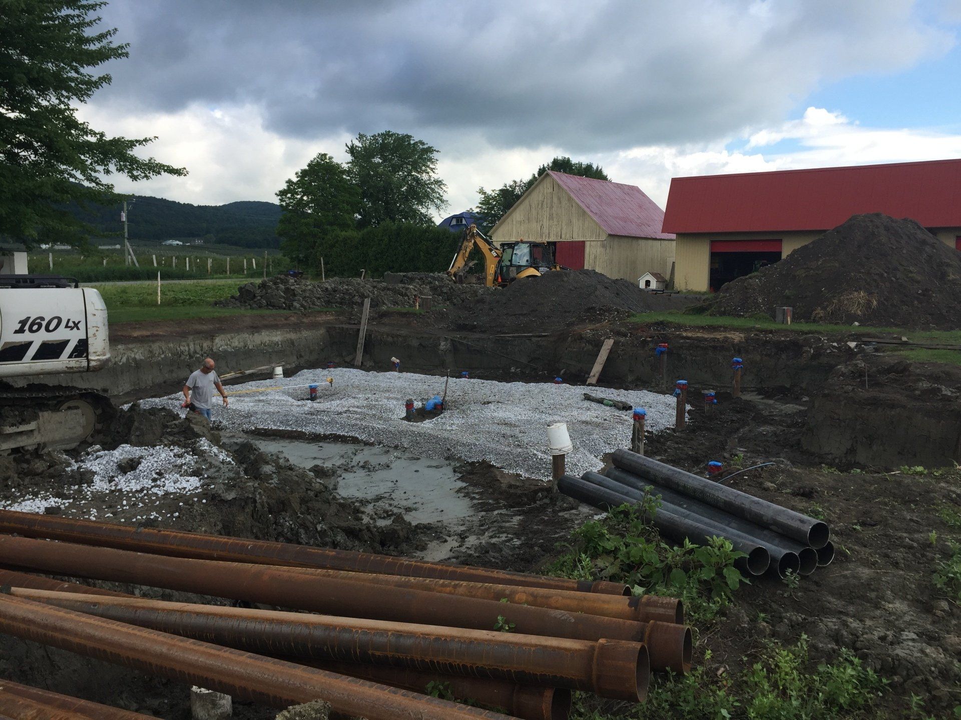 Un chantier de construction avec beaucoup de tuyaux et une grange rouge en arrière-plan.