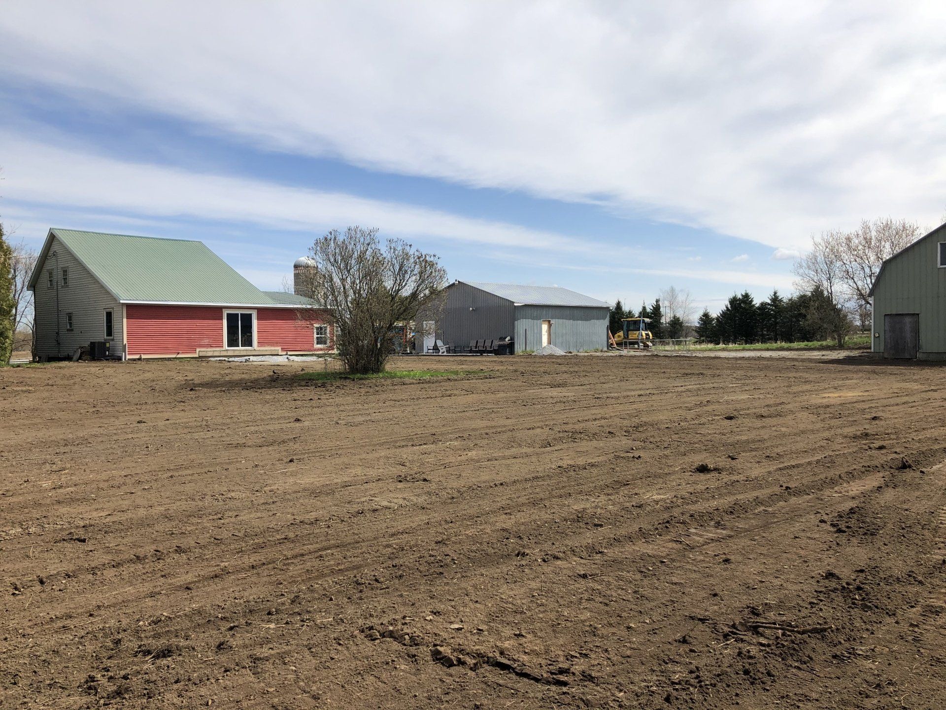 Une maison rouge avec un toit vert se trouve au milieu d’un champ de terre.