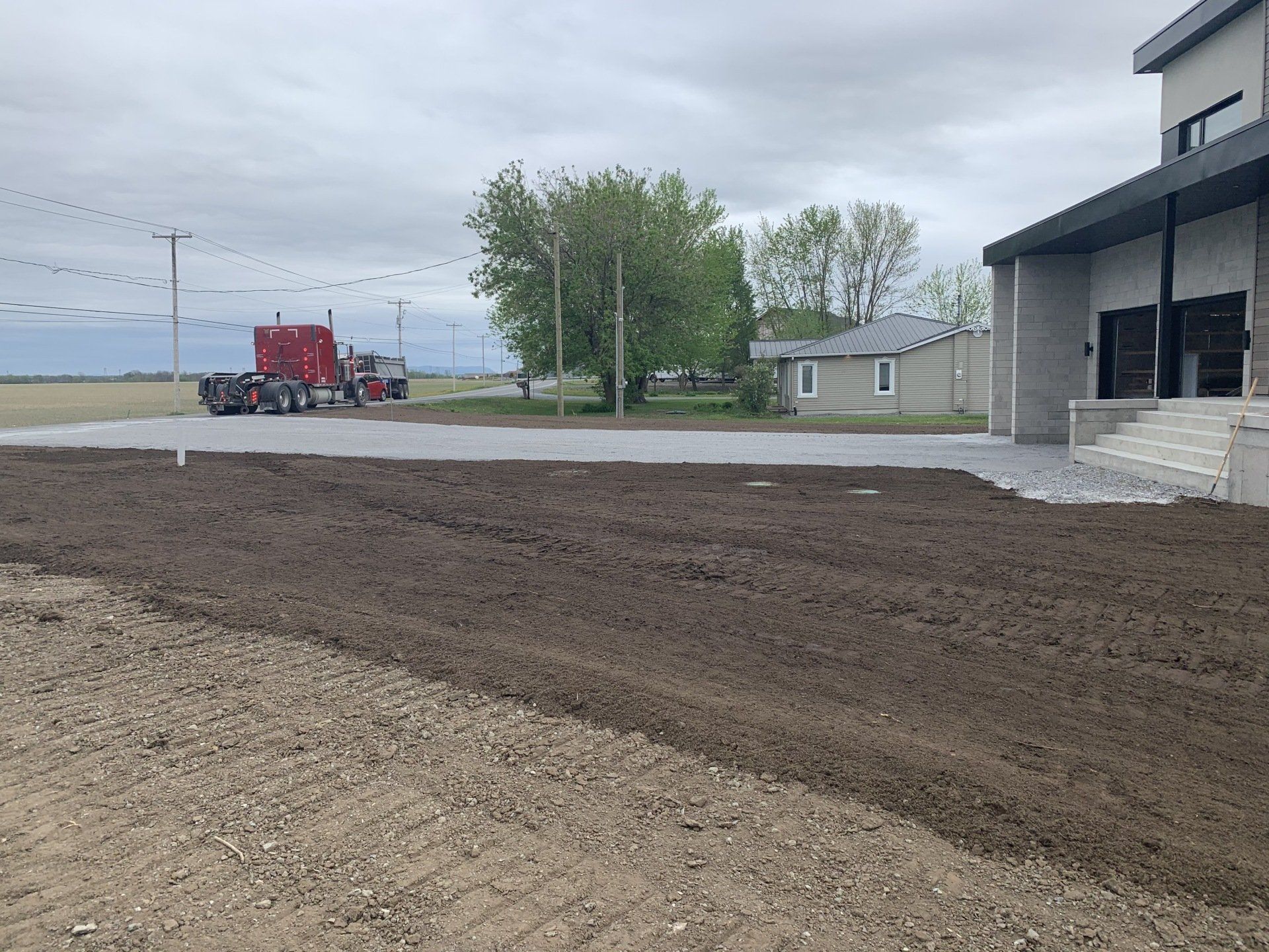 Un semi-remorque rouge est garé dans un terrain sale devant une maison.