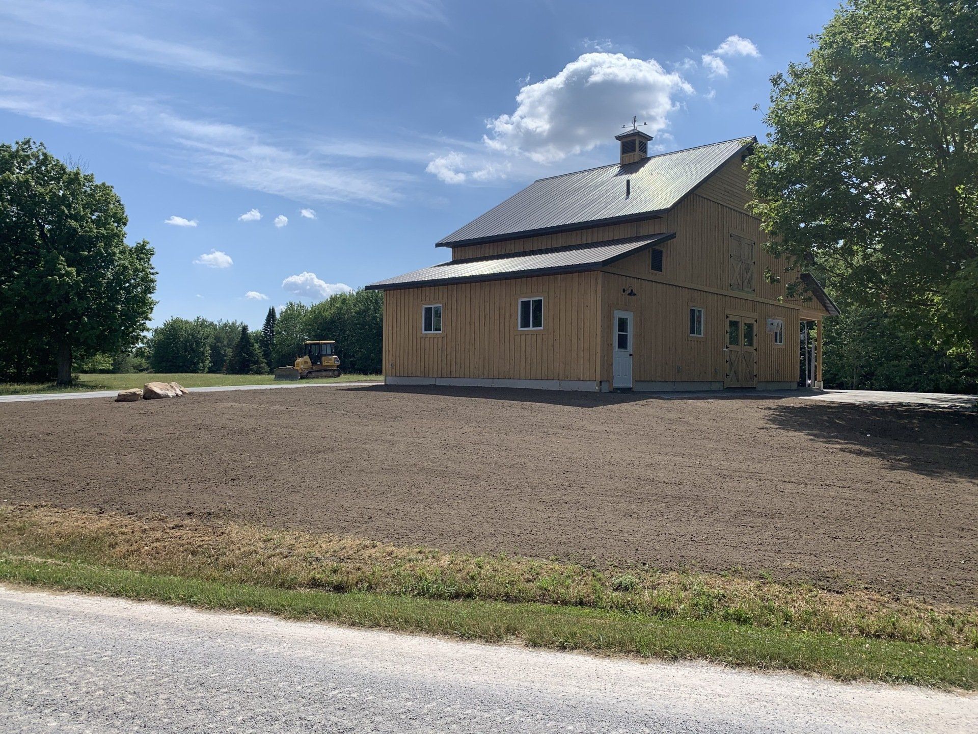 Une grande grange en bois se trouve au milieu d’un champ de terre.