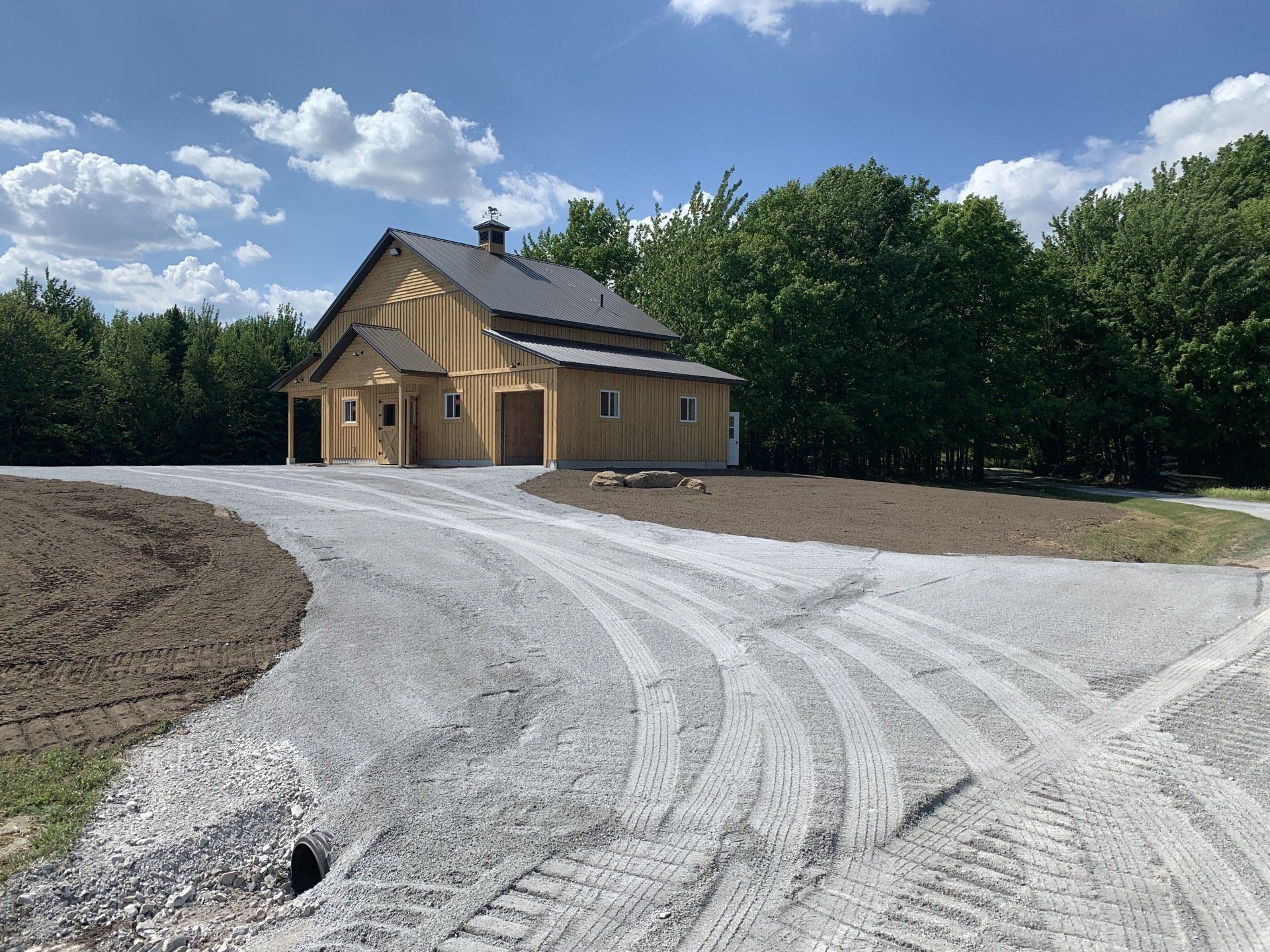 Une grande grange se trouve au sommet d’un chemin de terre entouré d’arbres.