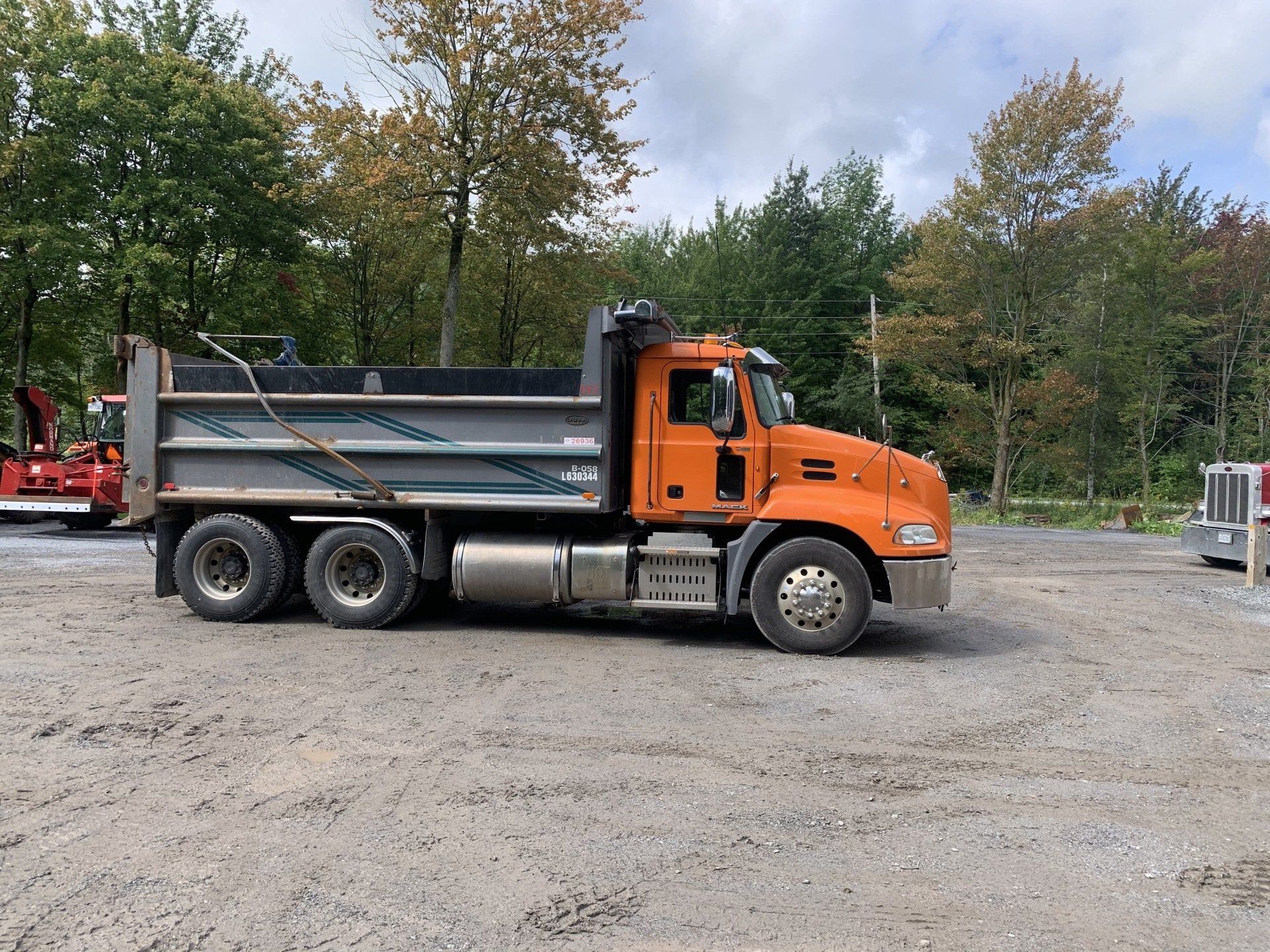 Un camion-benne orange est garé dans un terrain de gravier.