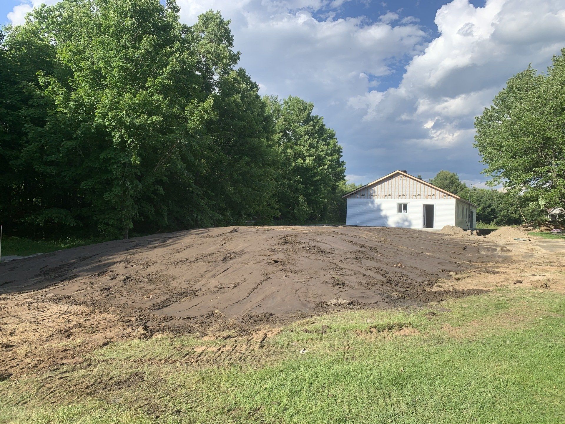 Une maison blanche se dresse au milieu d’un champ de terre entouré d’arbres.