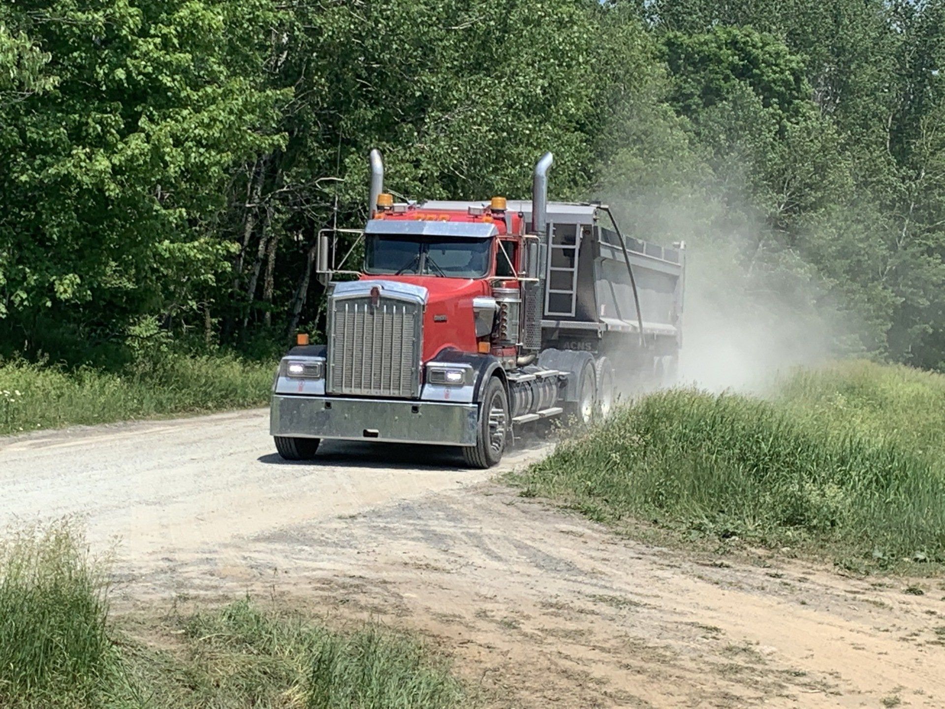 Un semi-remorque rouge roule sur un chemin de terre.