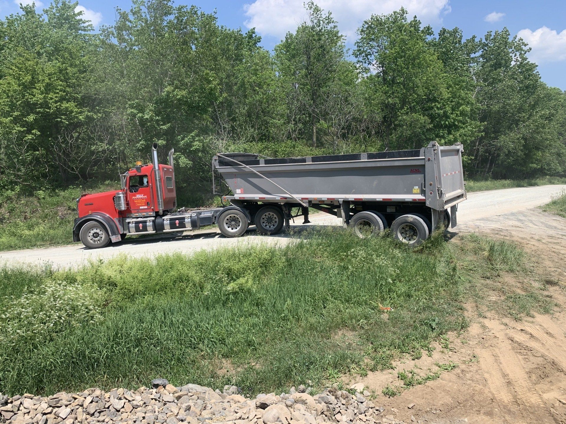 Un camion-benne rouge roule sur un chemin de terre.