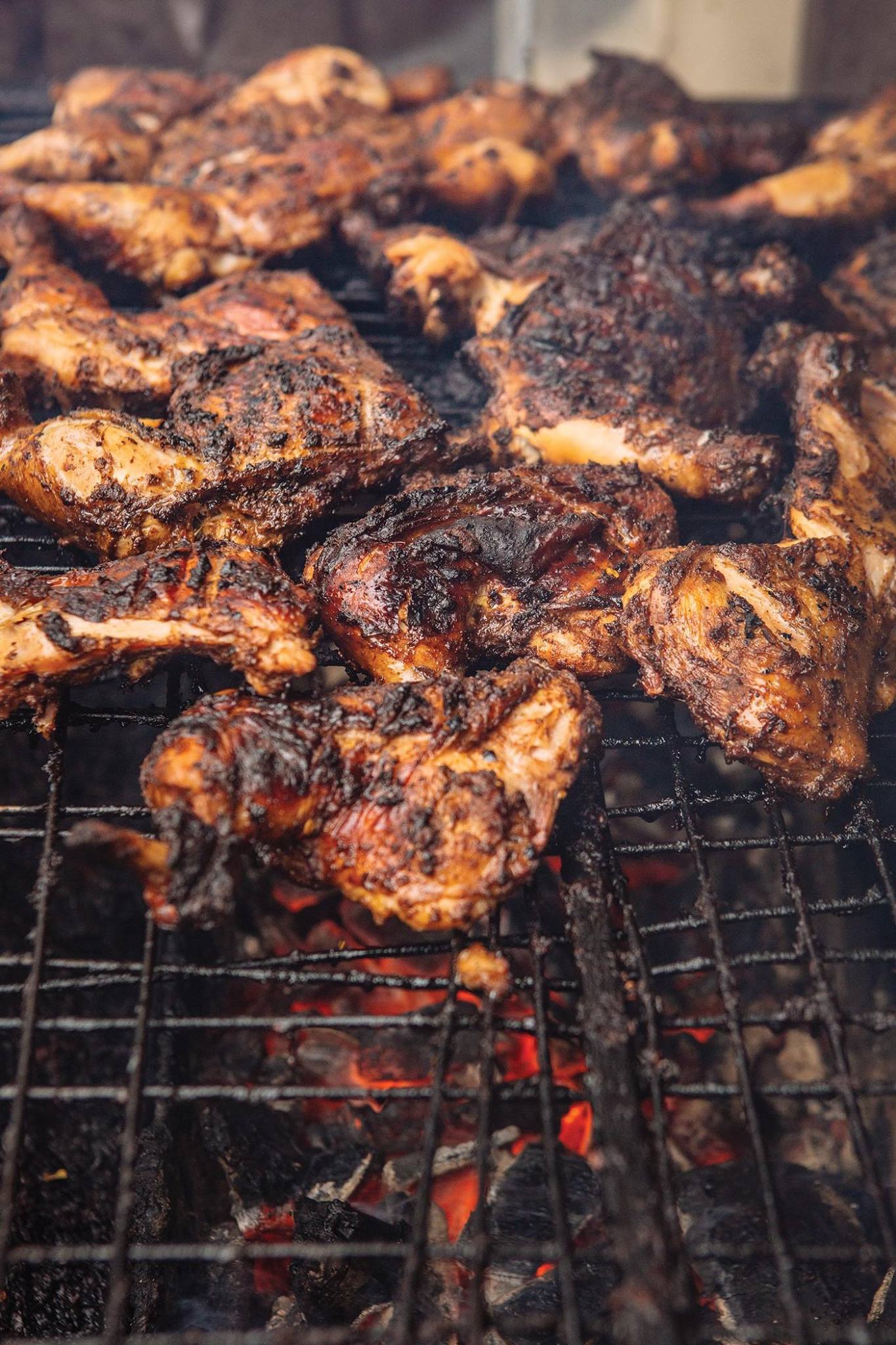 A bunch of chicken is cooking on a grill.