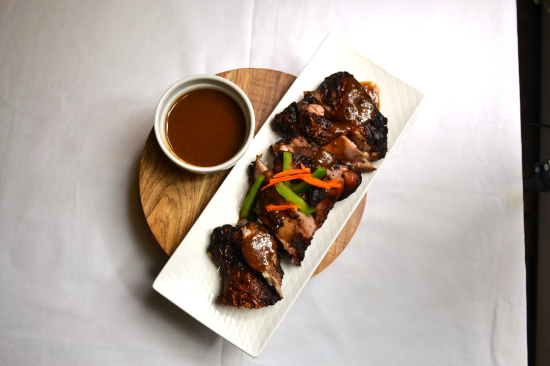 A white plate topped with meat and vegetables next to a bowl of sauce.