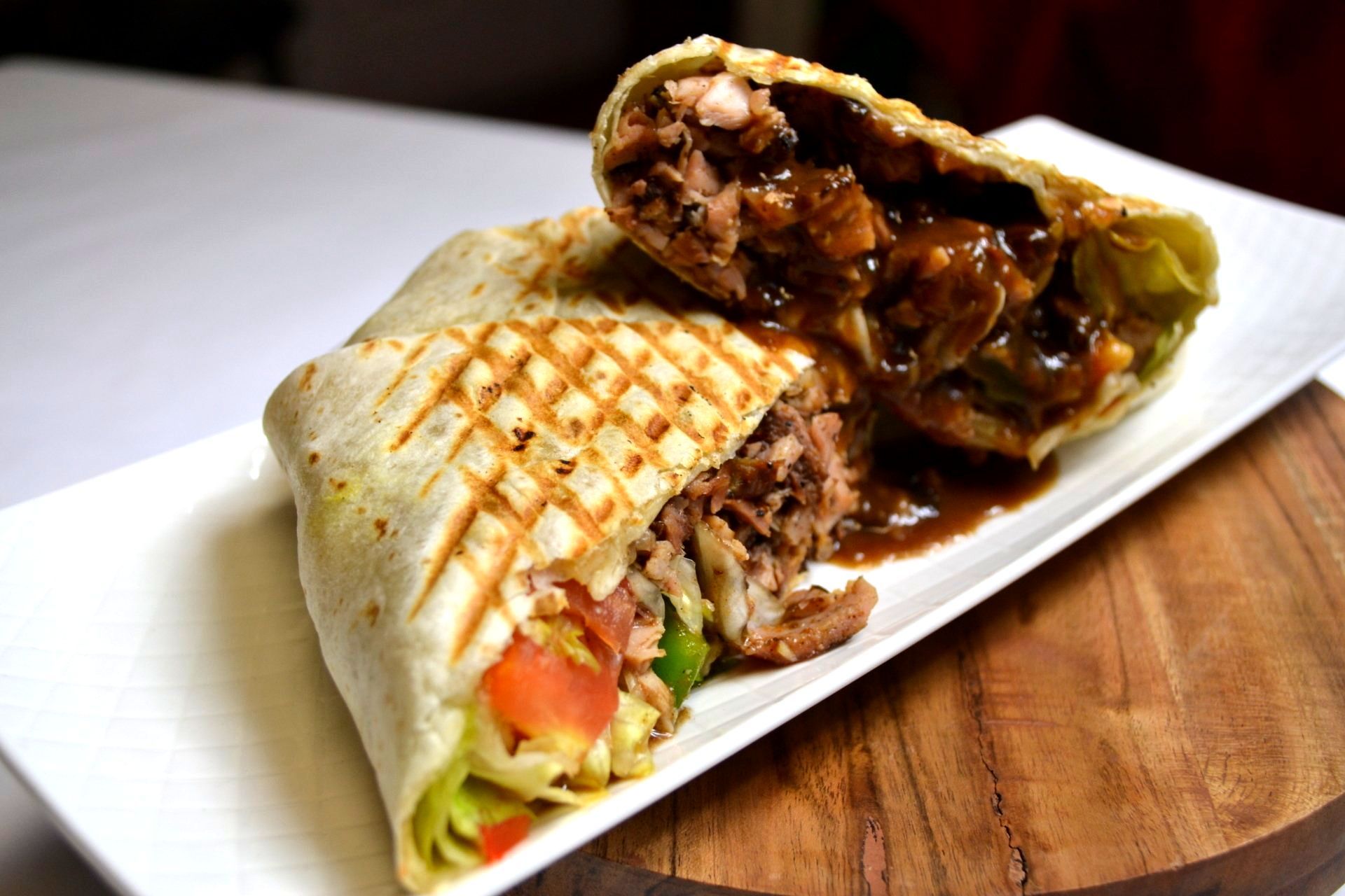 A burrito is cut in half on a white plate on a wooden table.