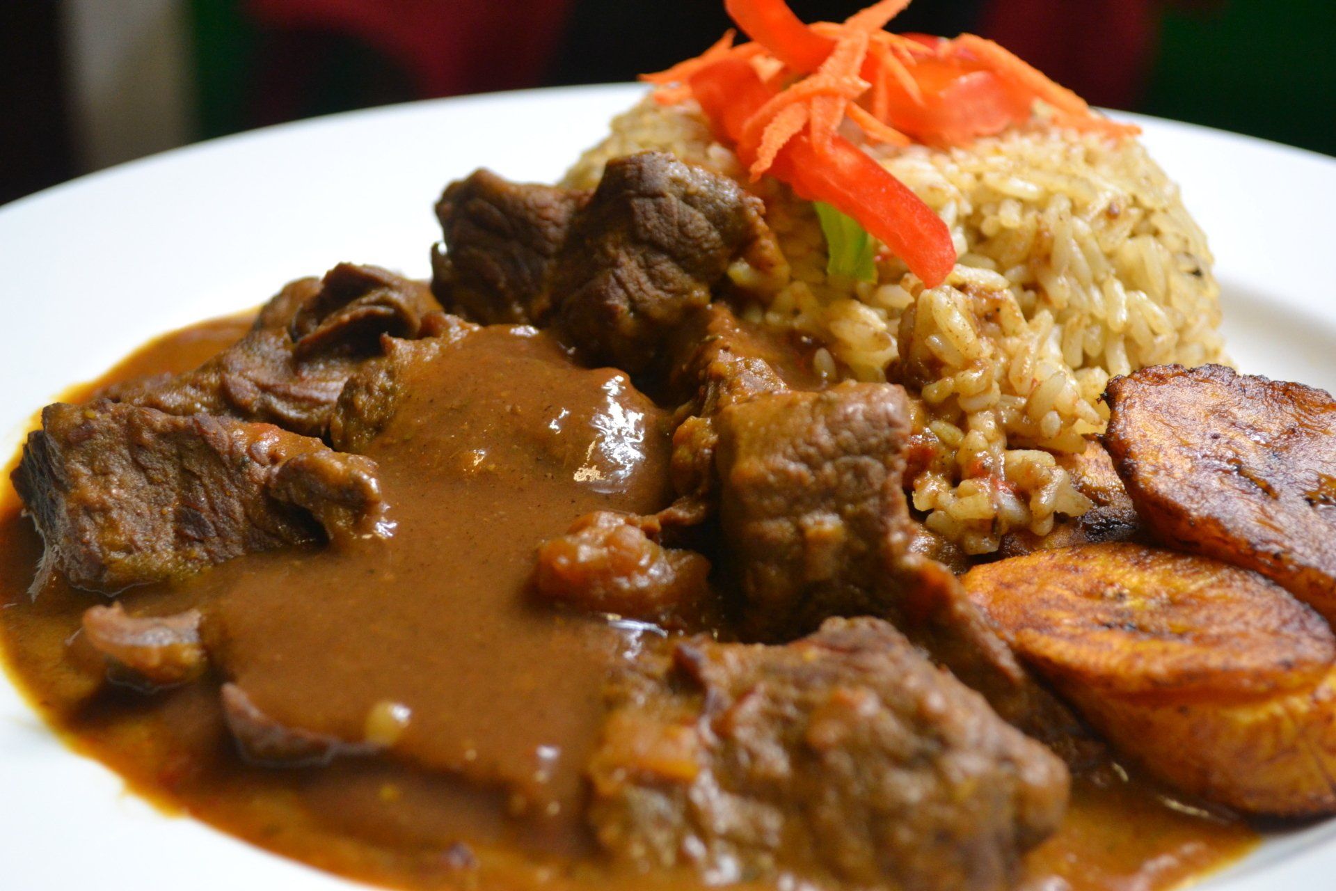 A white plate topped with meat , rice , and plantains.
