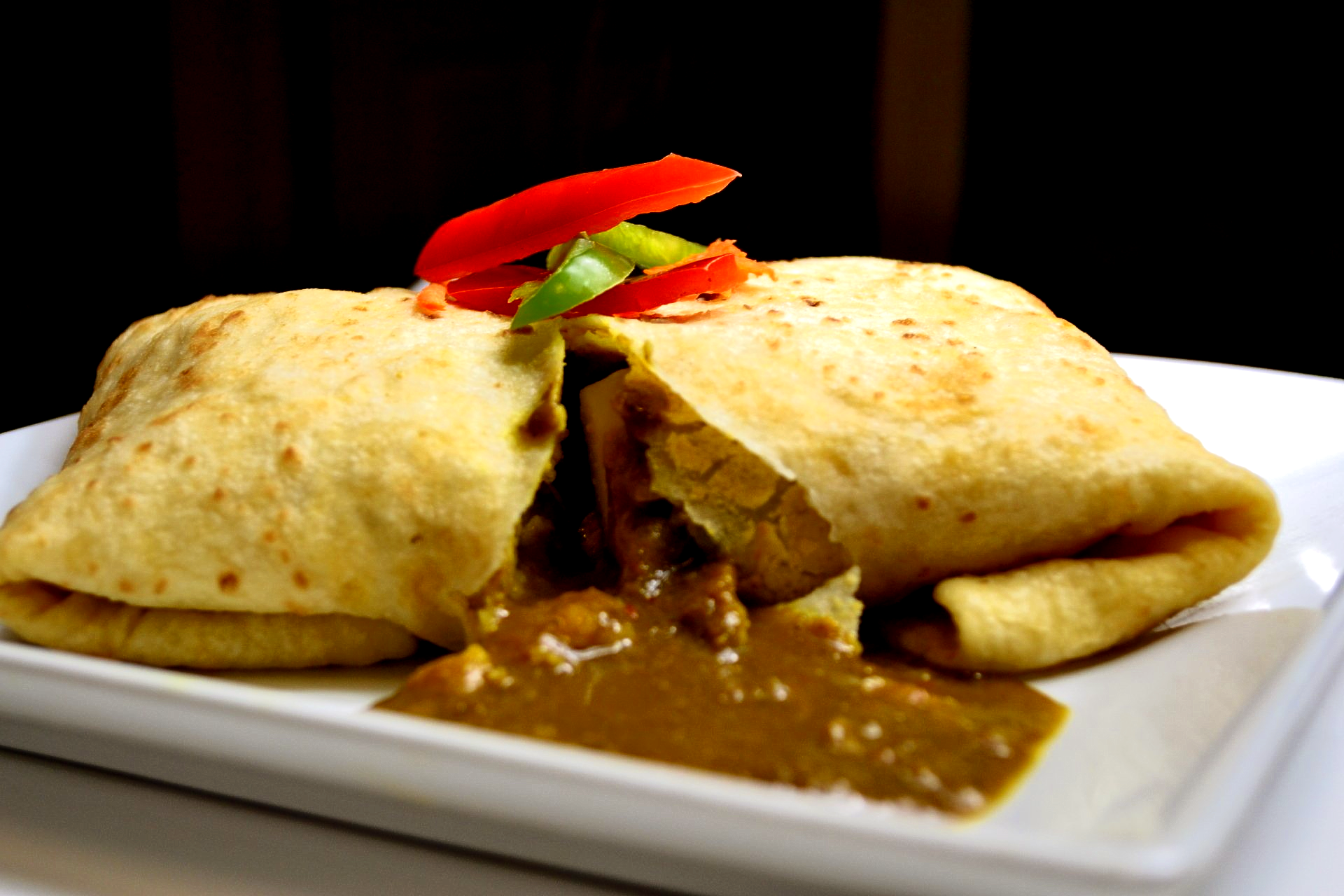 A burrito with curry and peppers on a white plate