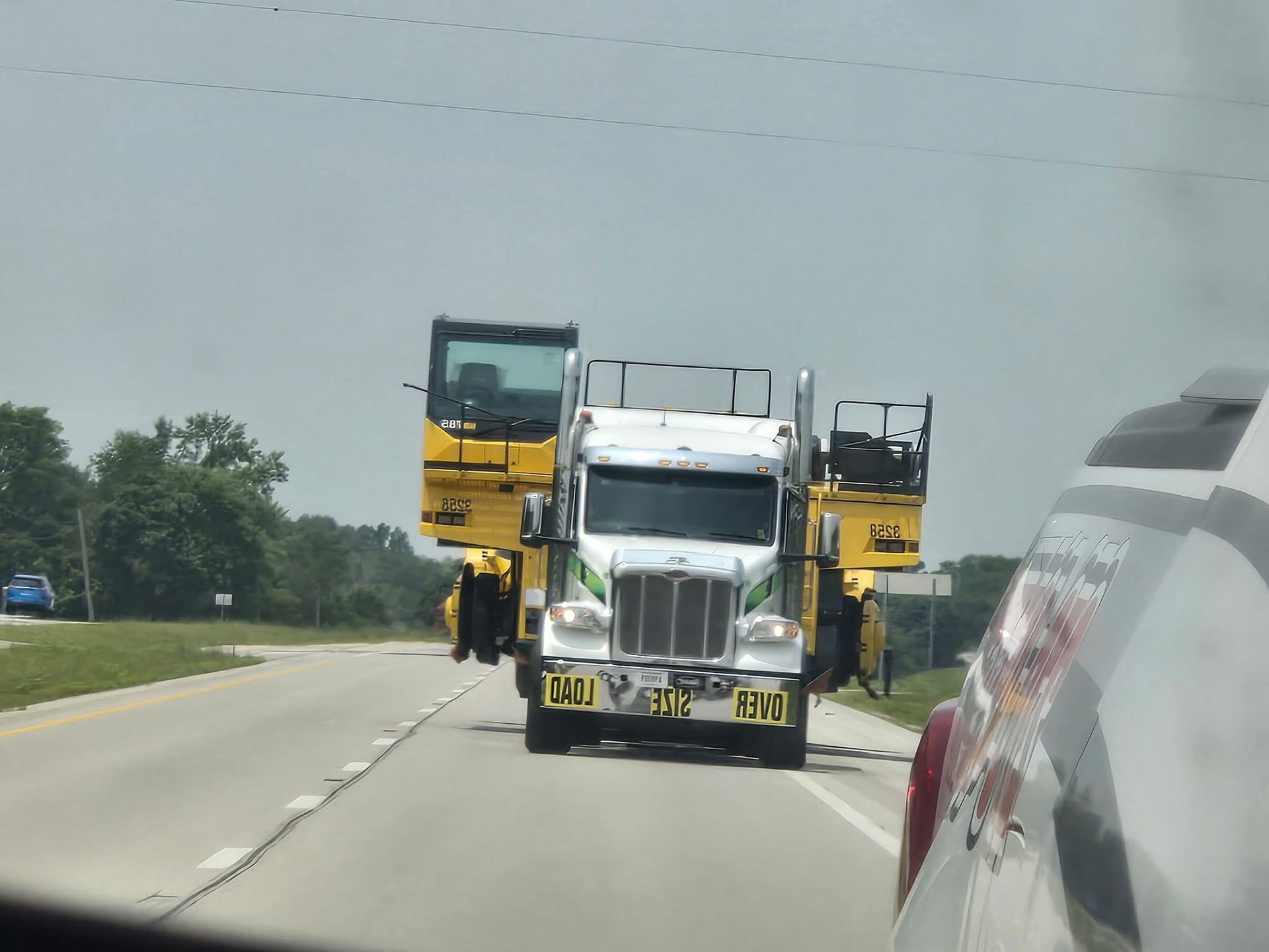 A large truck hauling a yellow road paving machine on a highway. Sunny day.