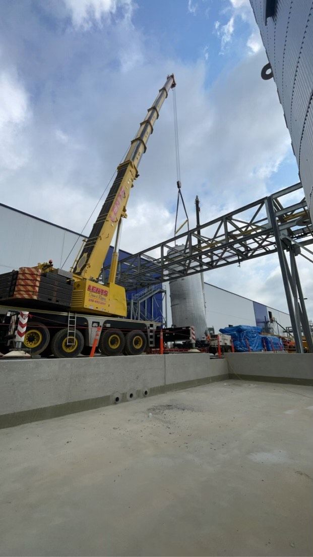 A yellow crane lifting a metal beam at a construction site on a cloudy day.