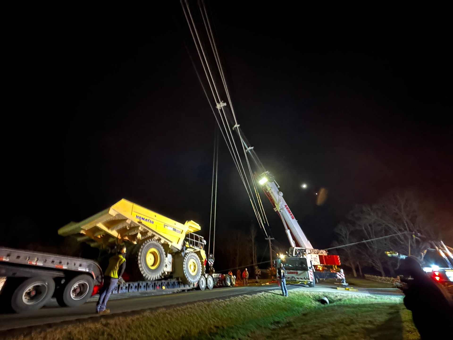 A large dump truck is being lifted by a crane at night.