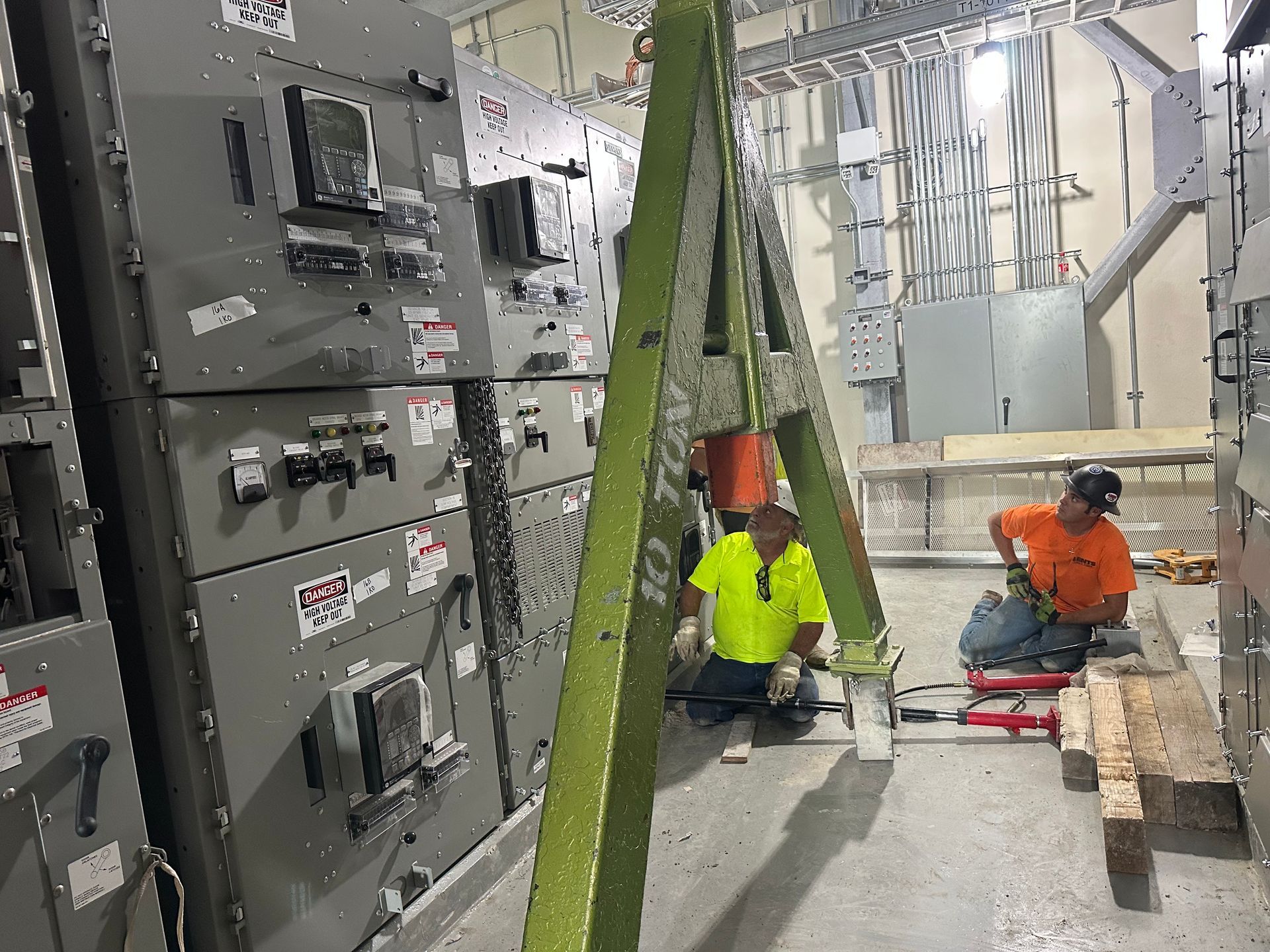 Two electricians working on electrical panels in a building, with a hoist.