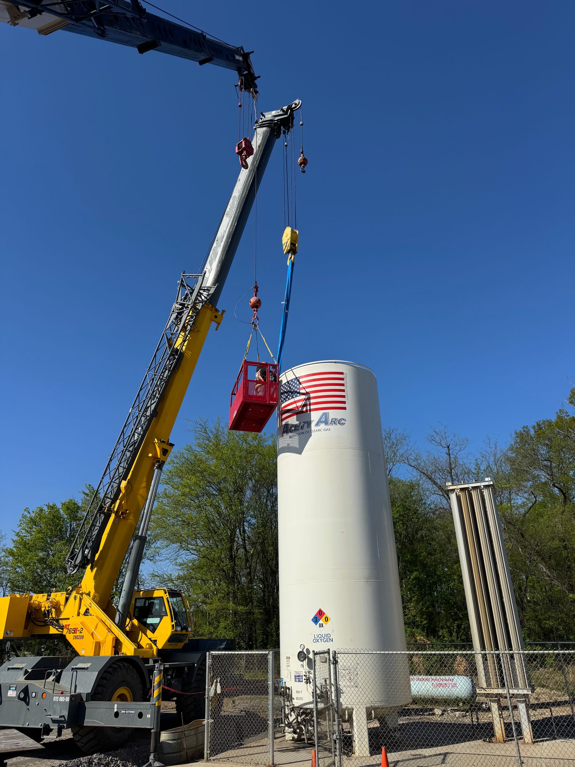 A crane lifting a red object above a white tank with blue sky in the background.