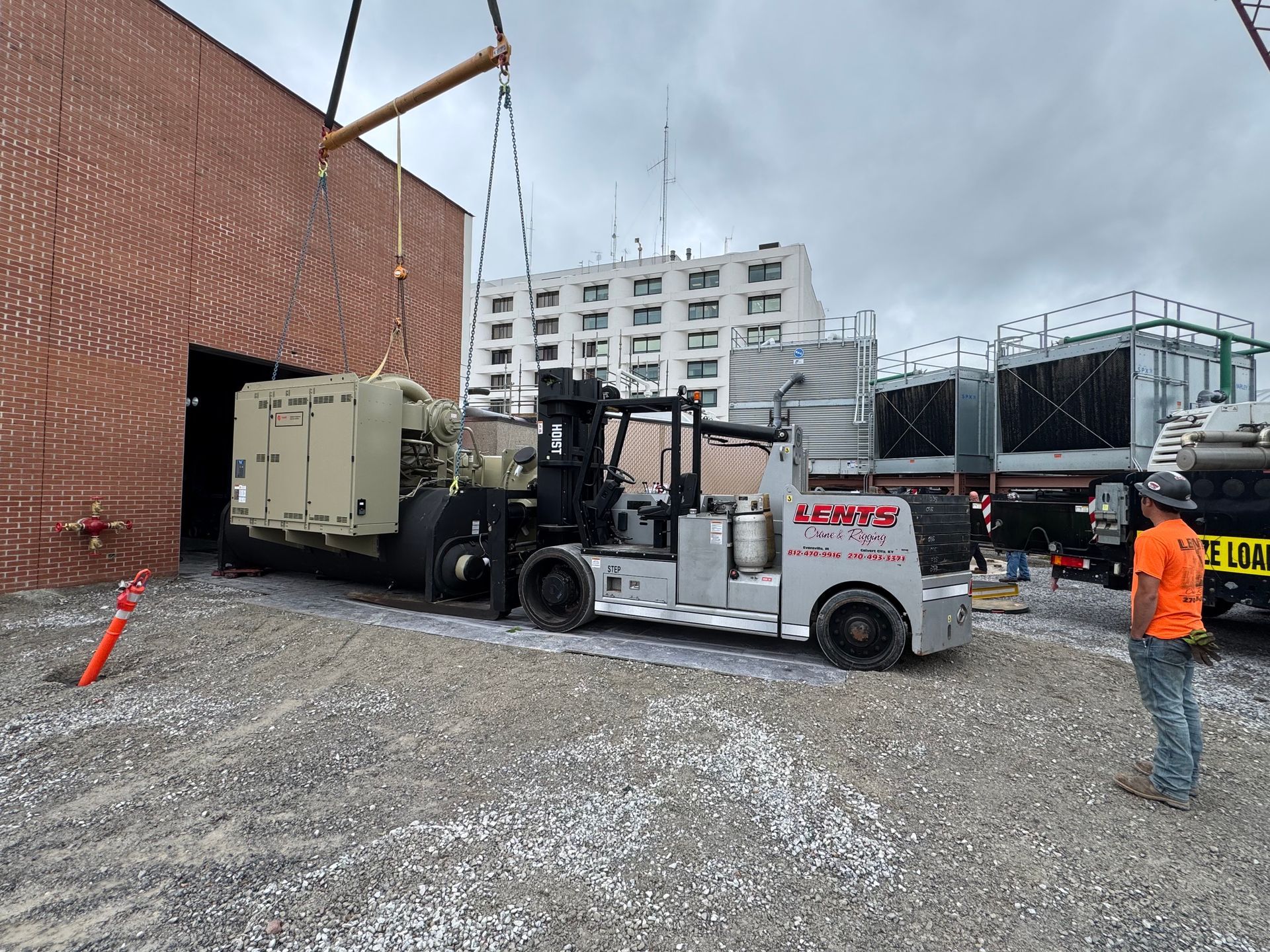 Forklift lifting a generator near a brick building with a worker observing.