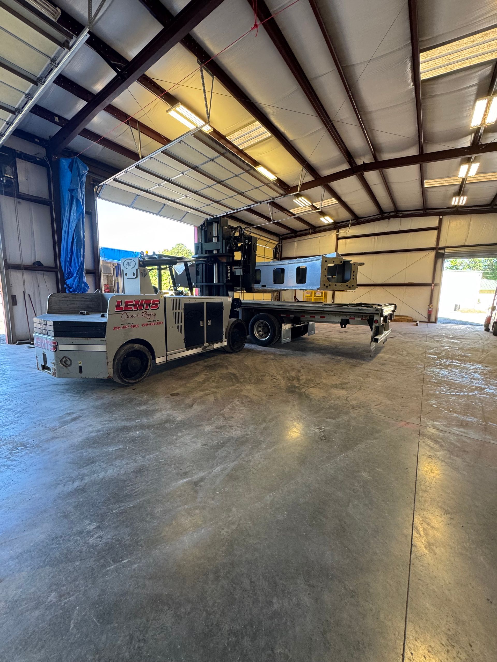 Large industrial machine on a trailer inside a metal building; gray and black, open doorway.