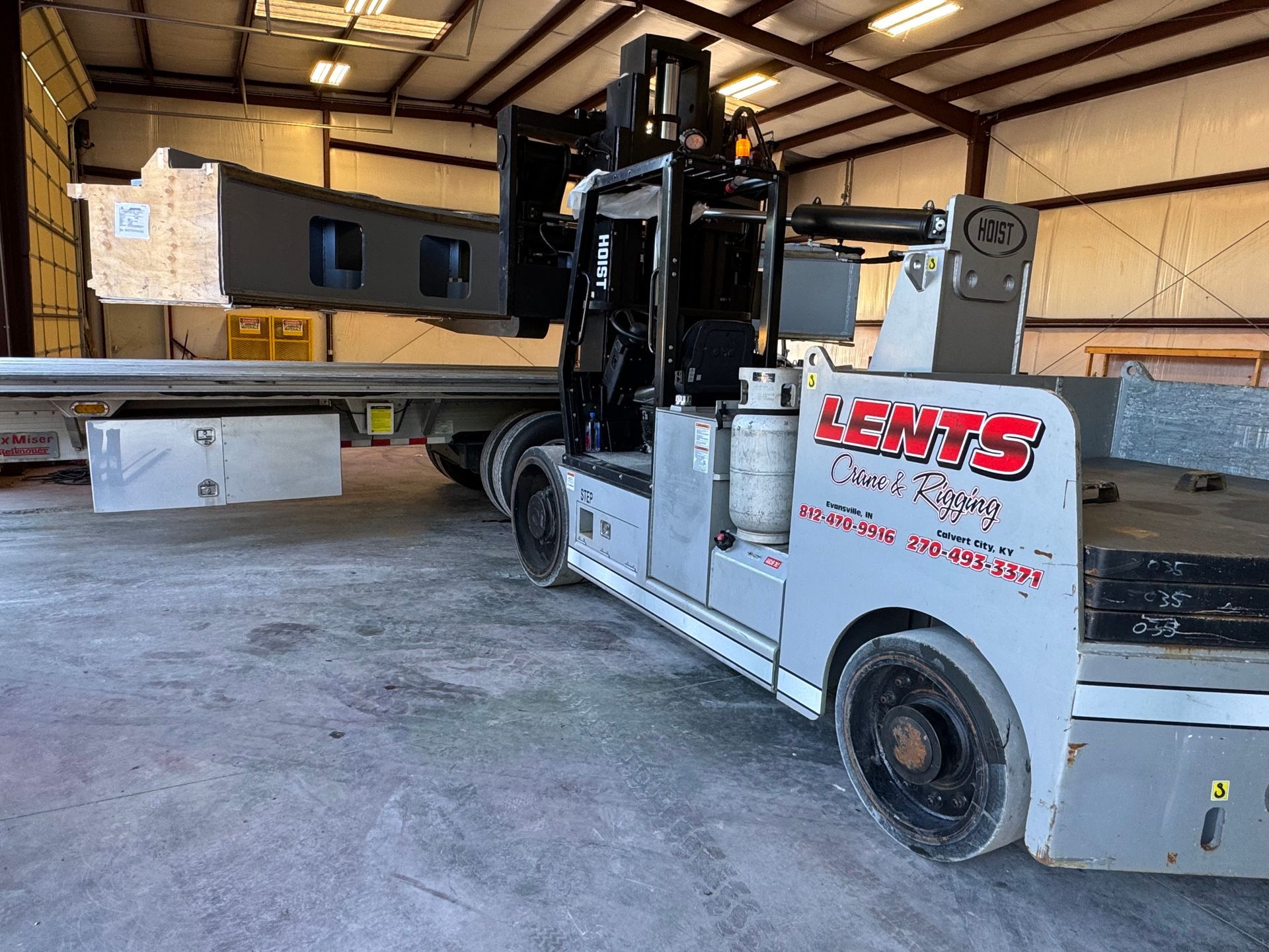 Forklift loading large concrete beams onto a trailer in a warehouse.